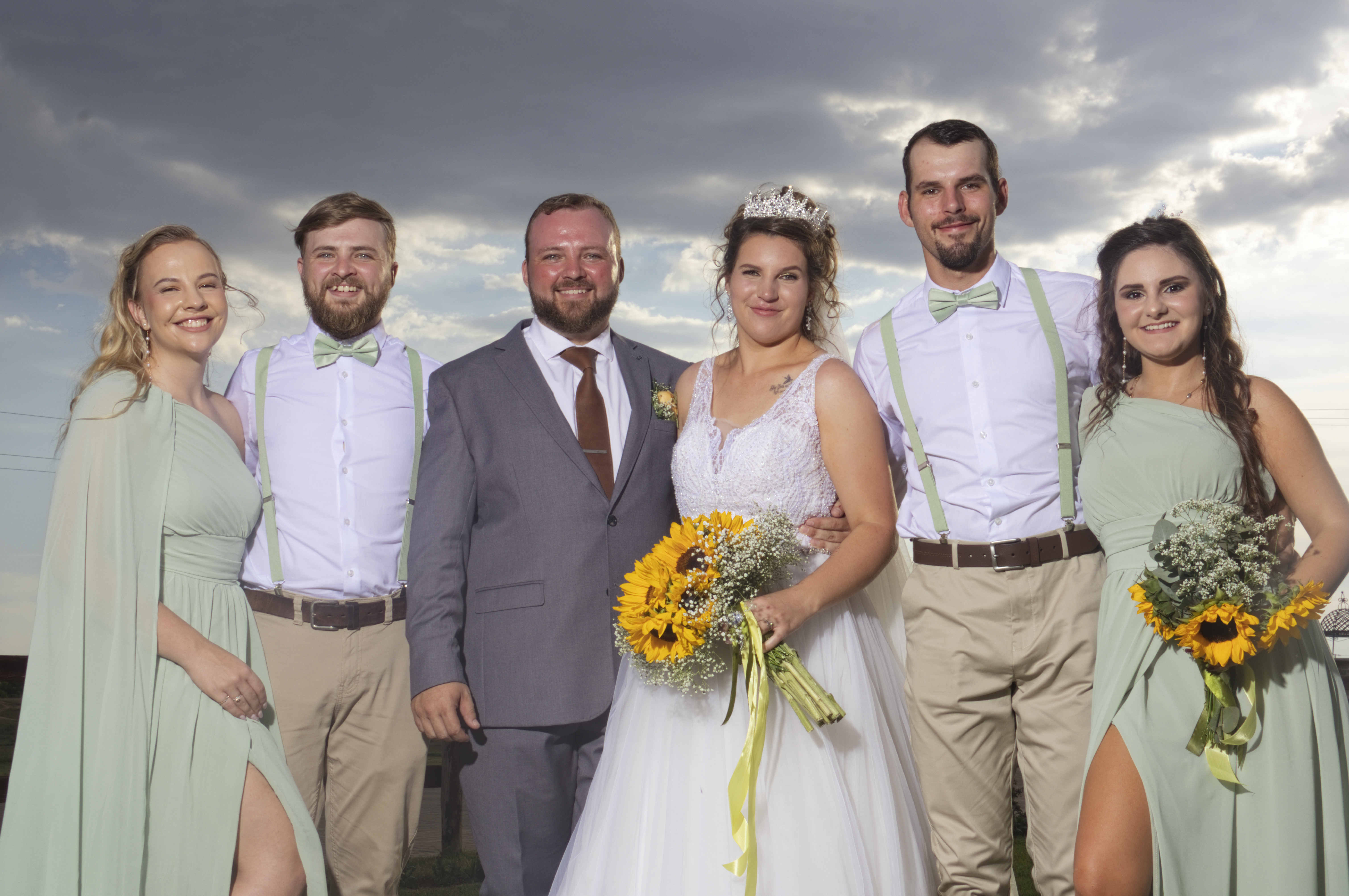 Bride and groom with their sage-green bridal party and sunflower bouquets