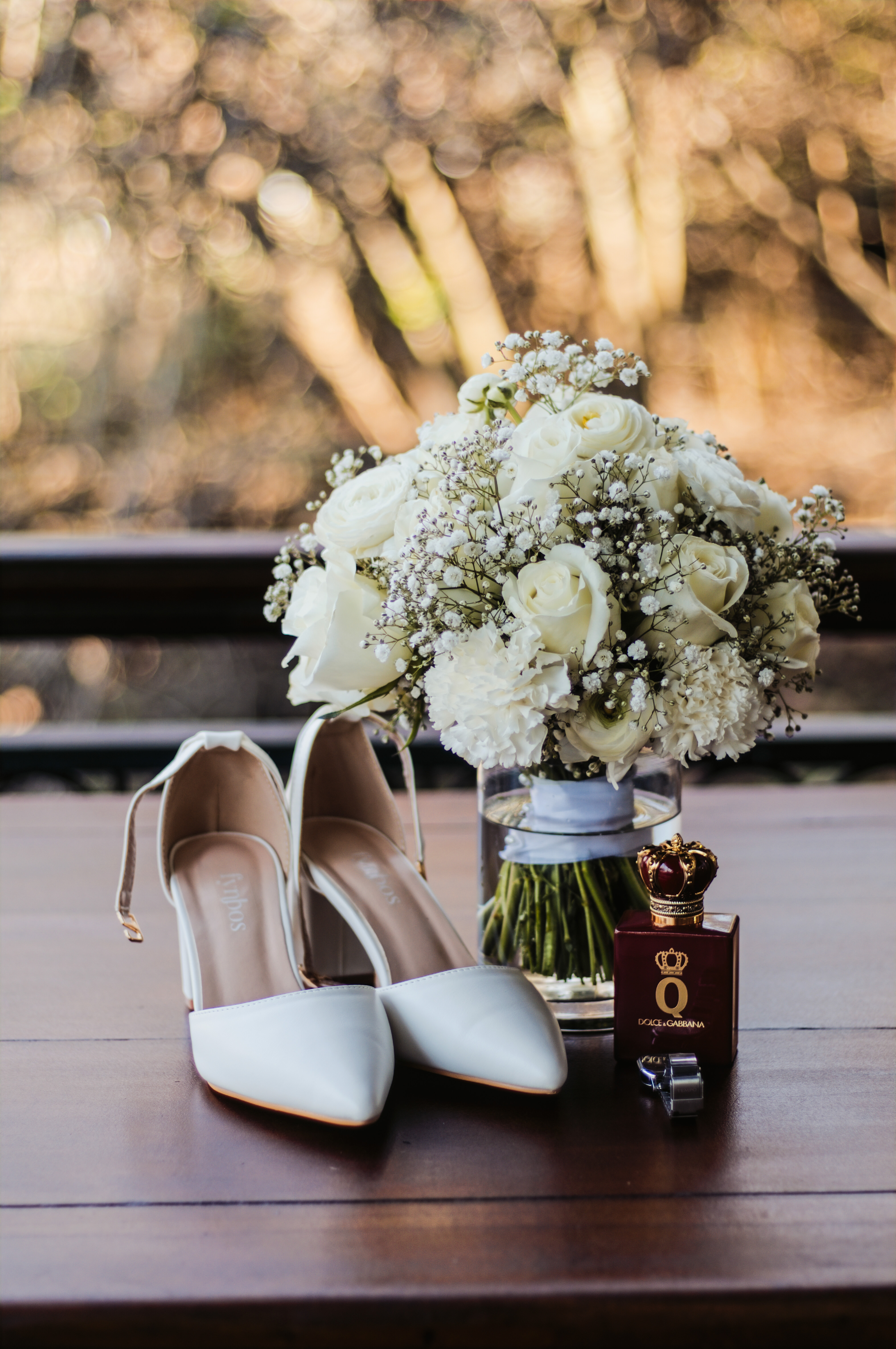 Bridal shoes beside a white rose bouquet and perfume