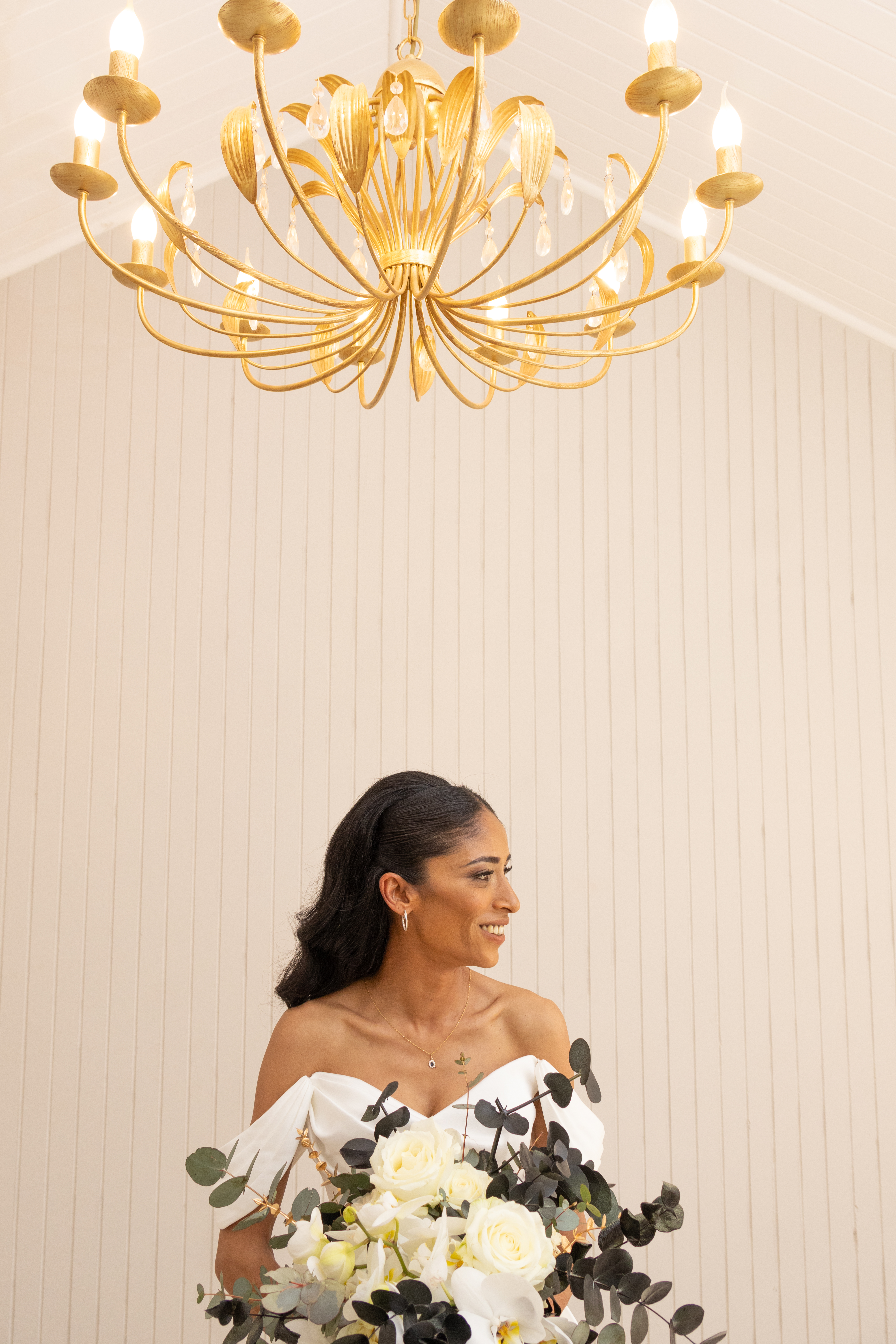 Smiling bride with a white bouquet beneath a gold chandelier