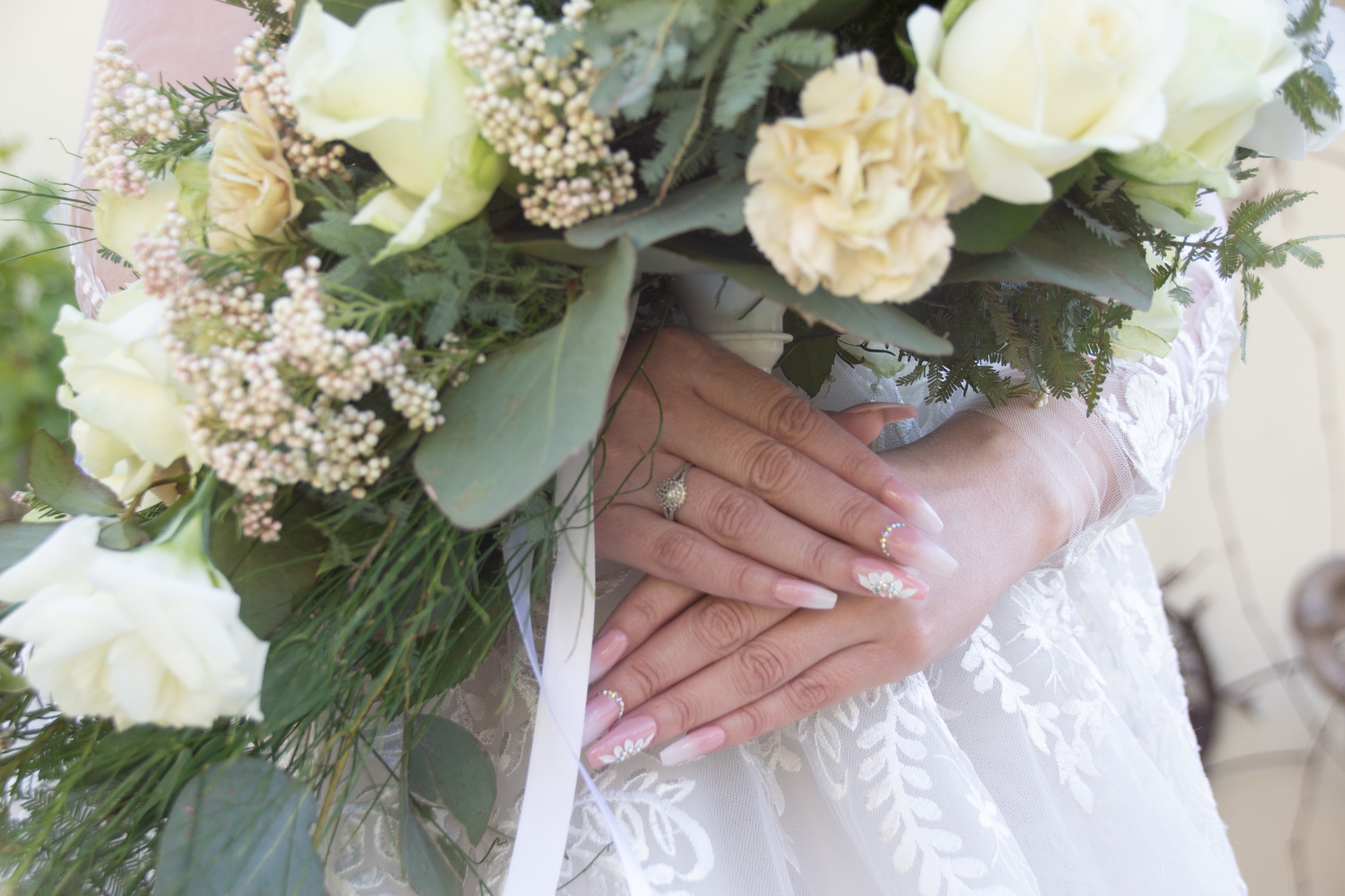Bride's hands with engagement ring resting on a white rose bouquet