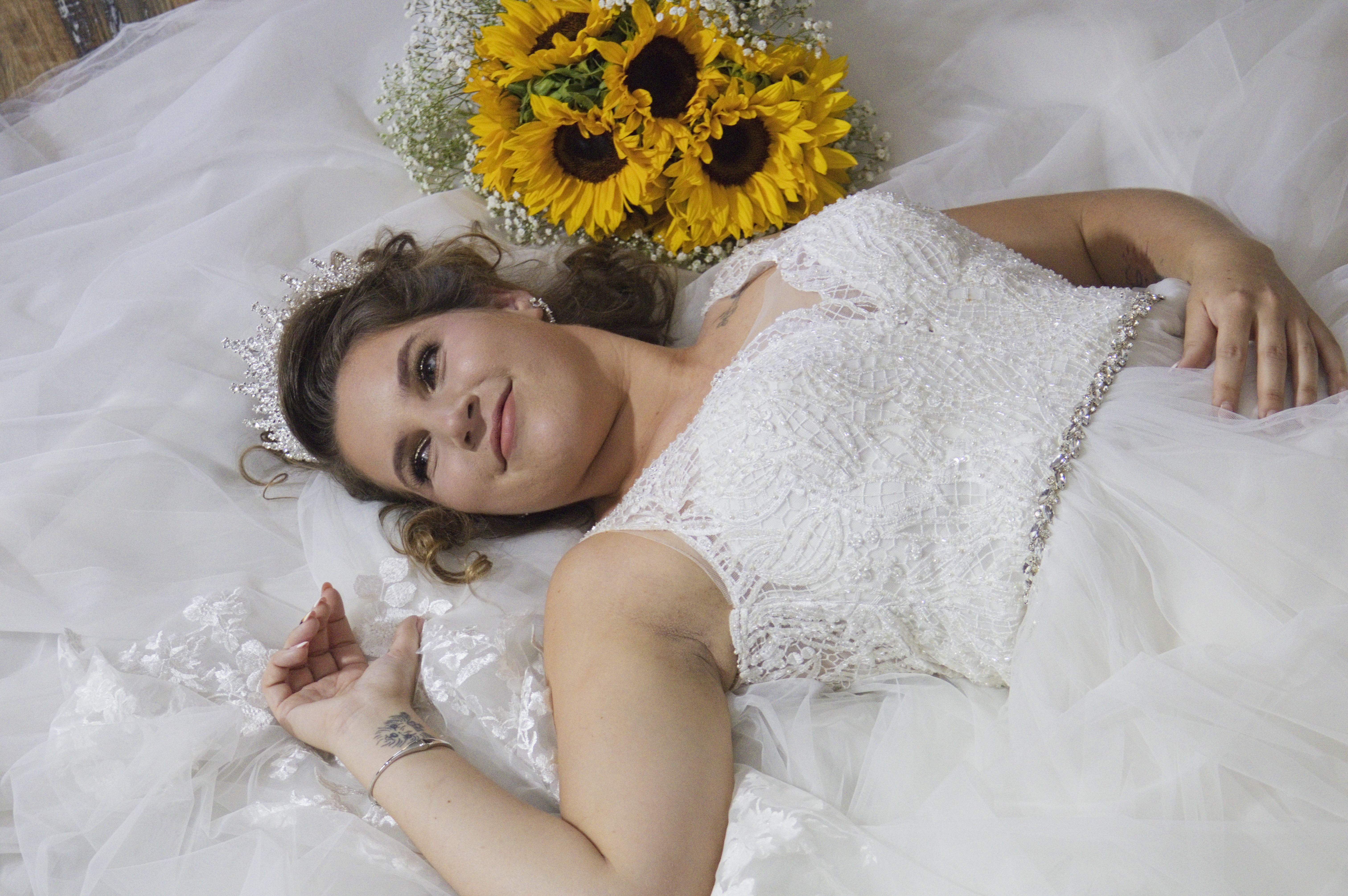 Bride lying in her tulle gown beside a sunflower bouquet