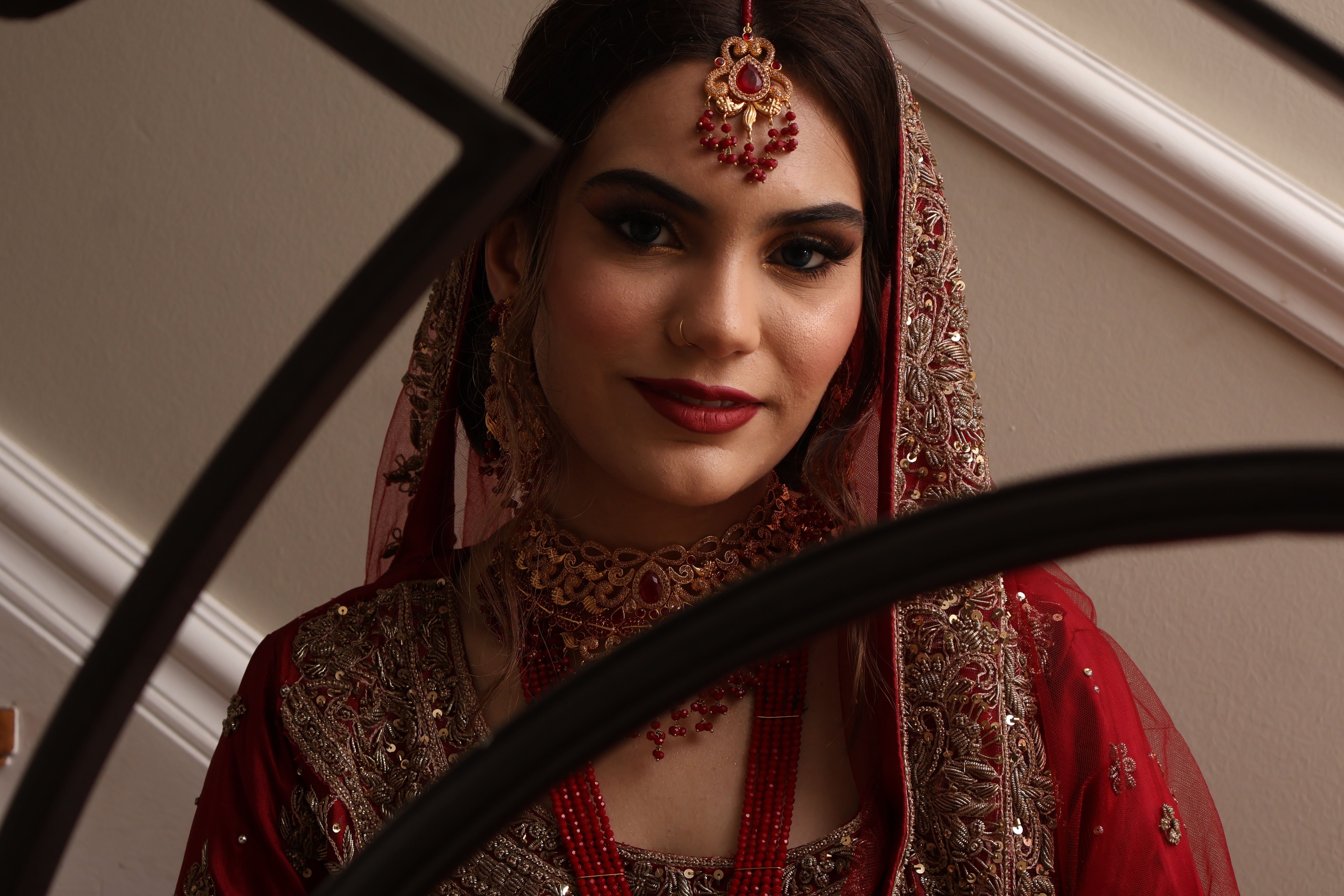 Bride with maang tikka framed through an iron stair railing