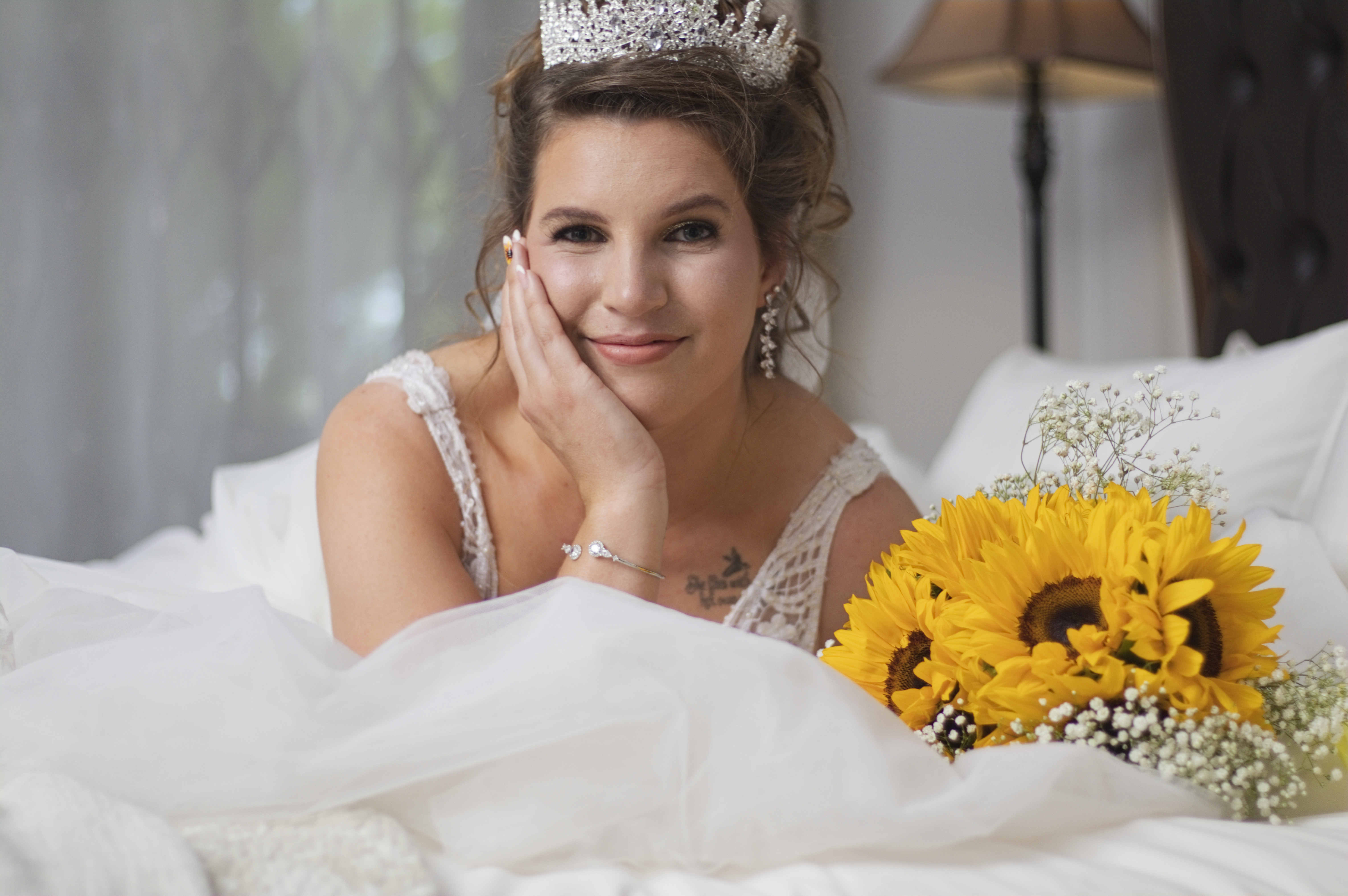 Smiling bride in a tiara resting on the bed beside sunflowers
