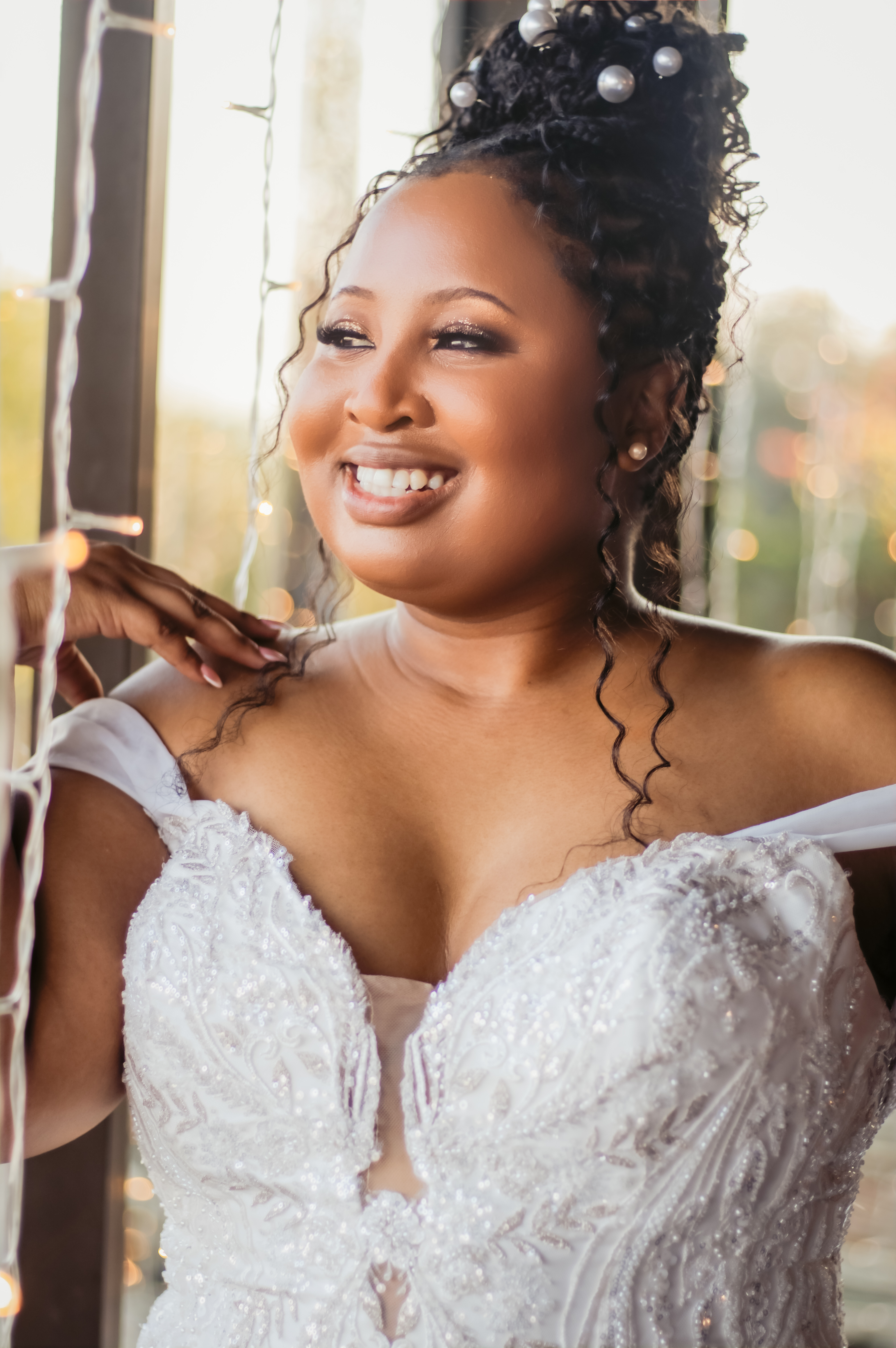 Joyful bride with pearl-studded updo beside fairy lights