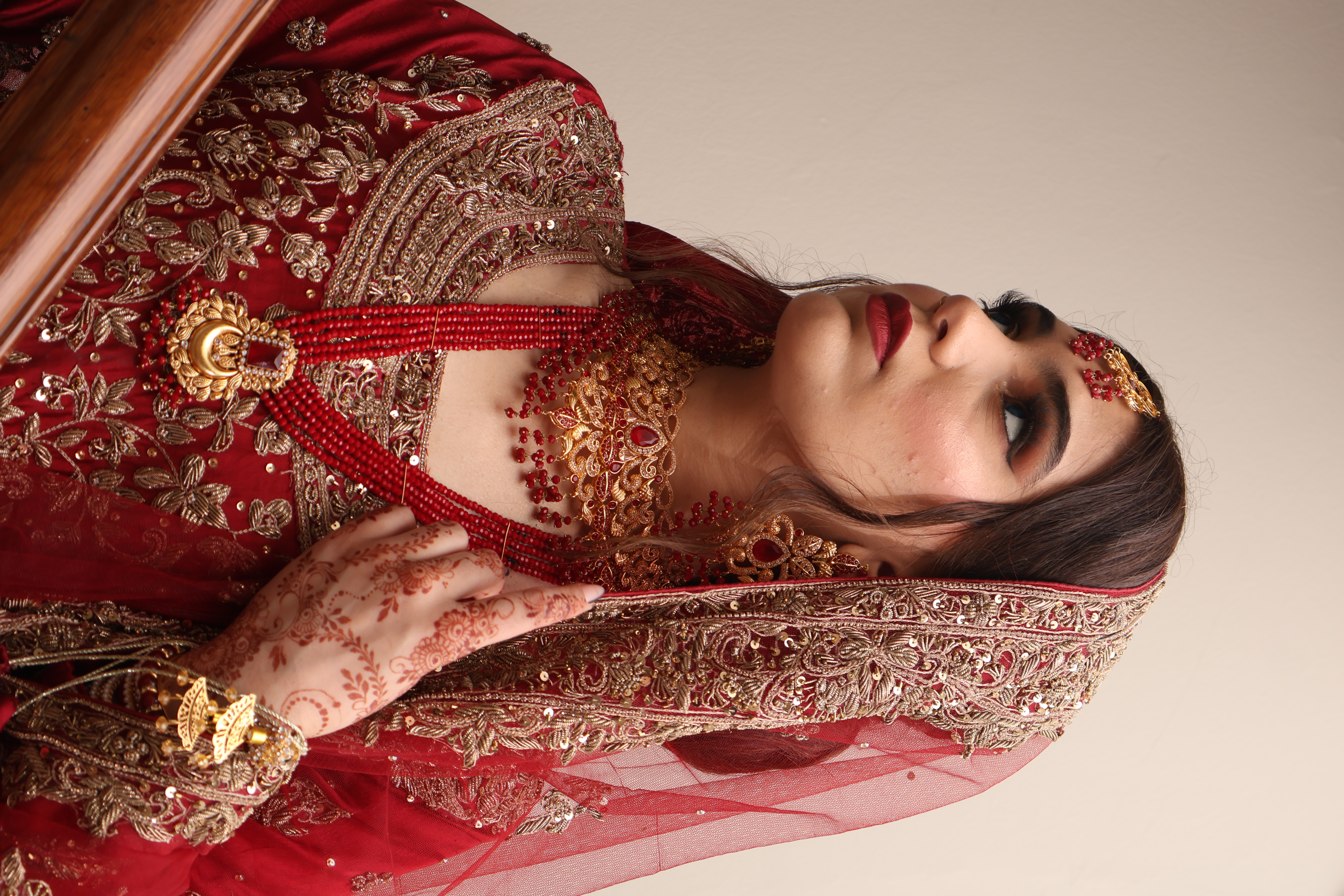 Bride in a red embroidered lehenga with gold jewellery and henna
