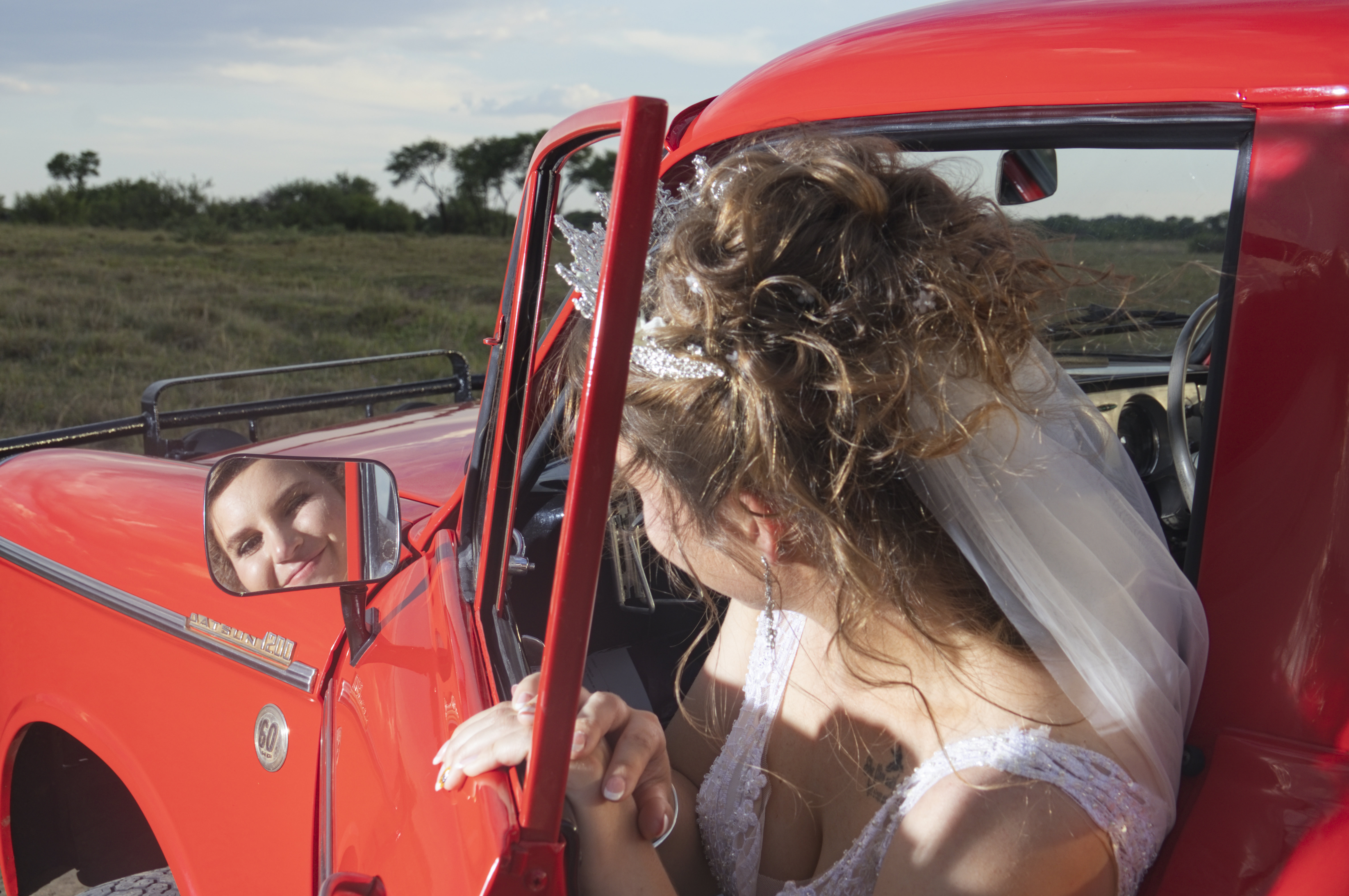 Bride smiling into the side mirror of a vintage red truck
