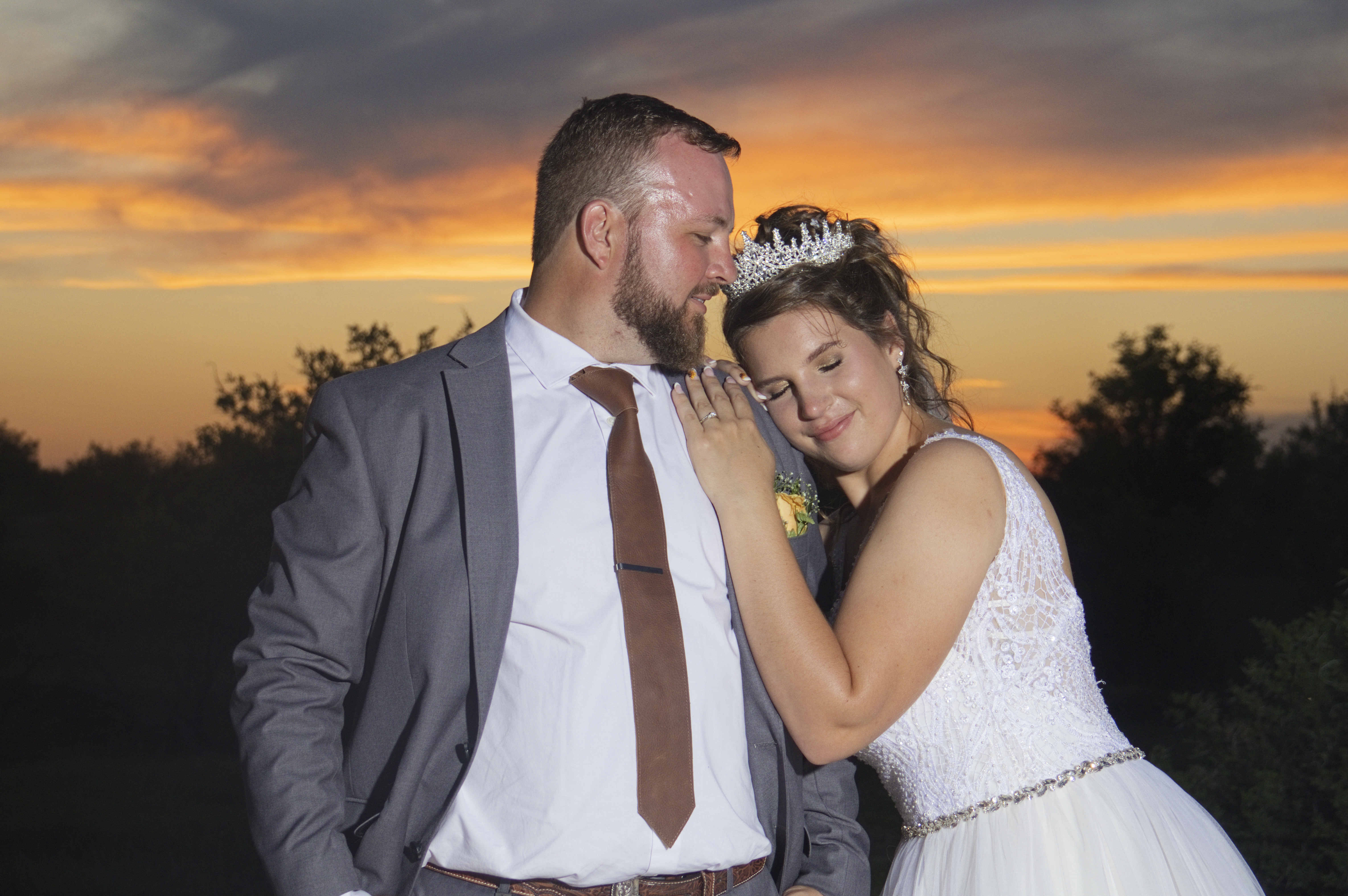 Bride resting her head on the groom's shoulder at sunset