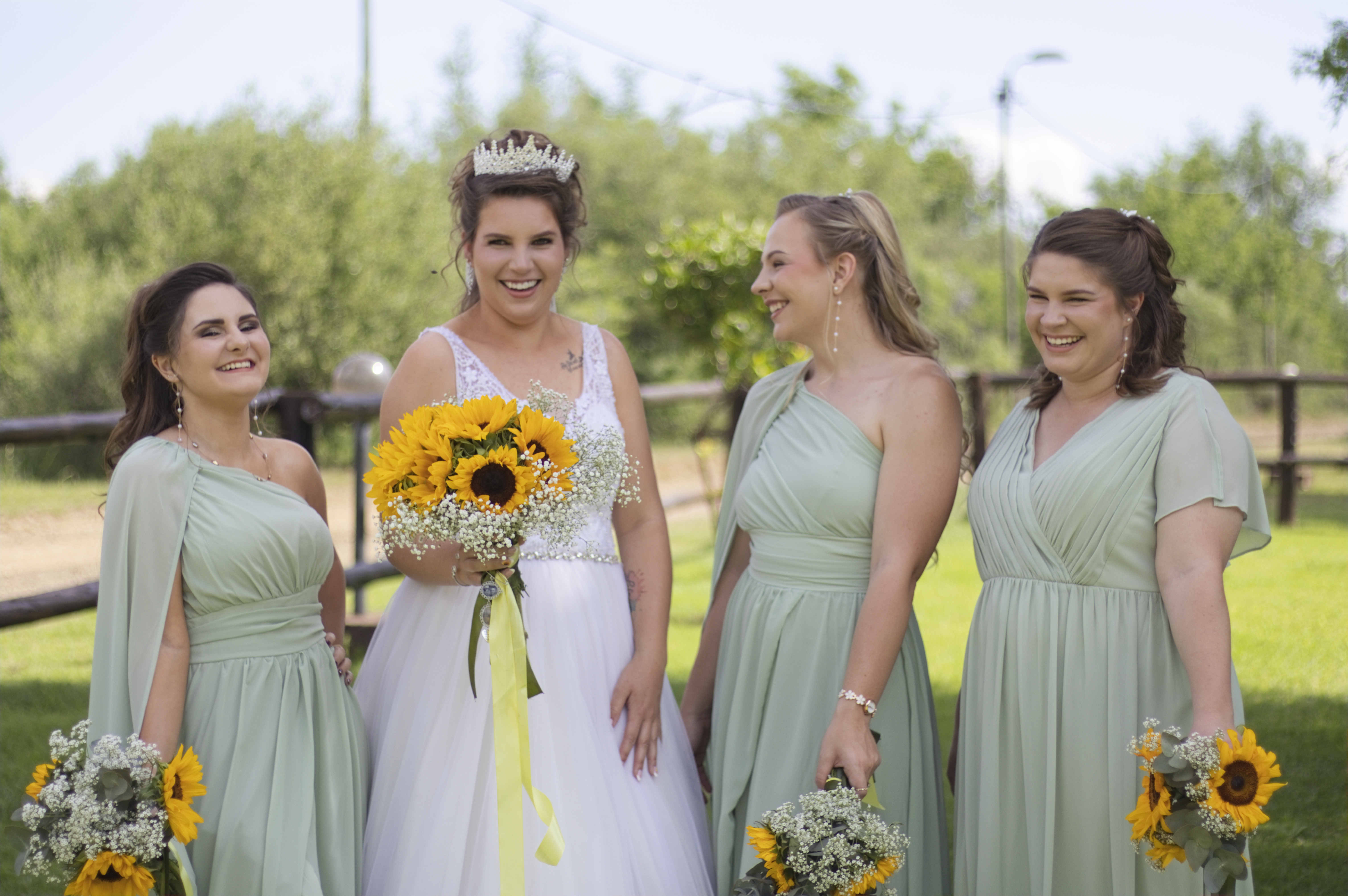 Bride laughing with her sage green bridesmaids holding sunflowers