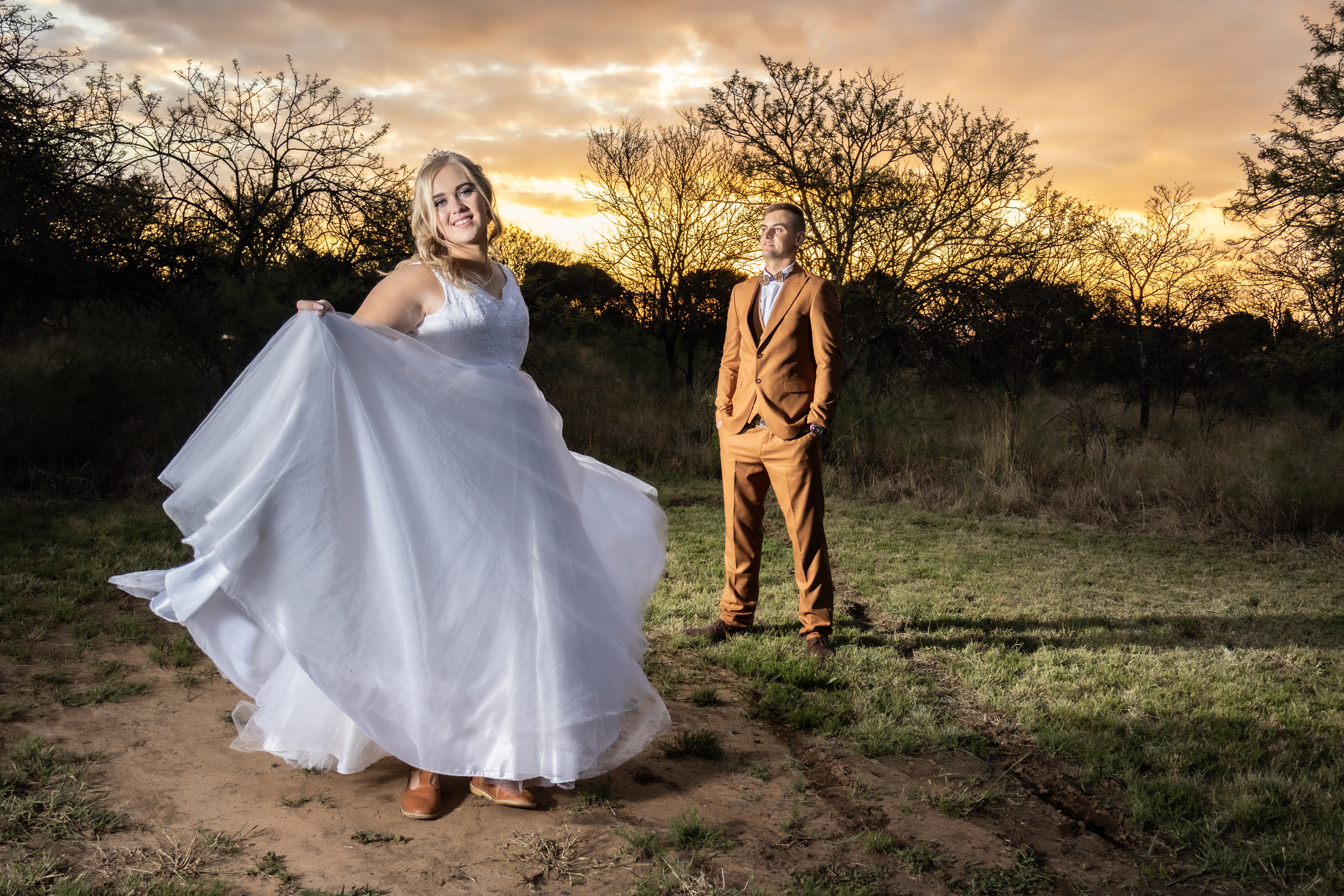 Bride twirling her gown as the groom stands in the golden sunset