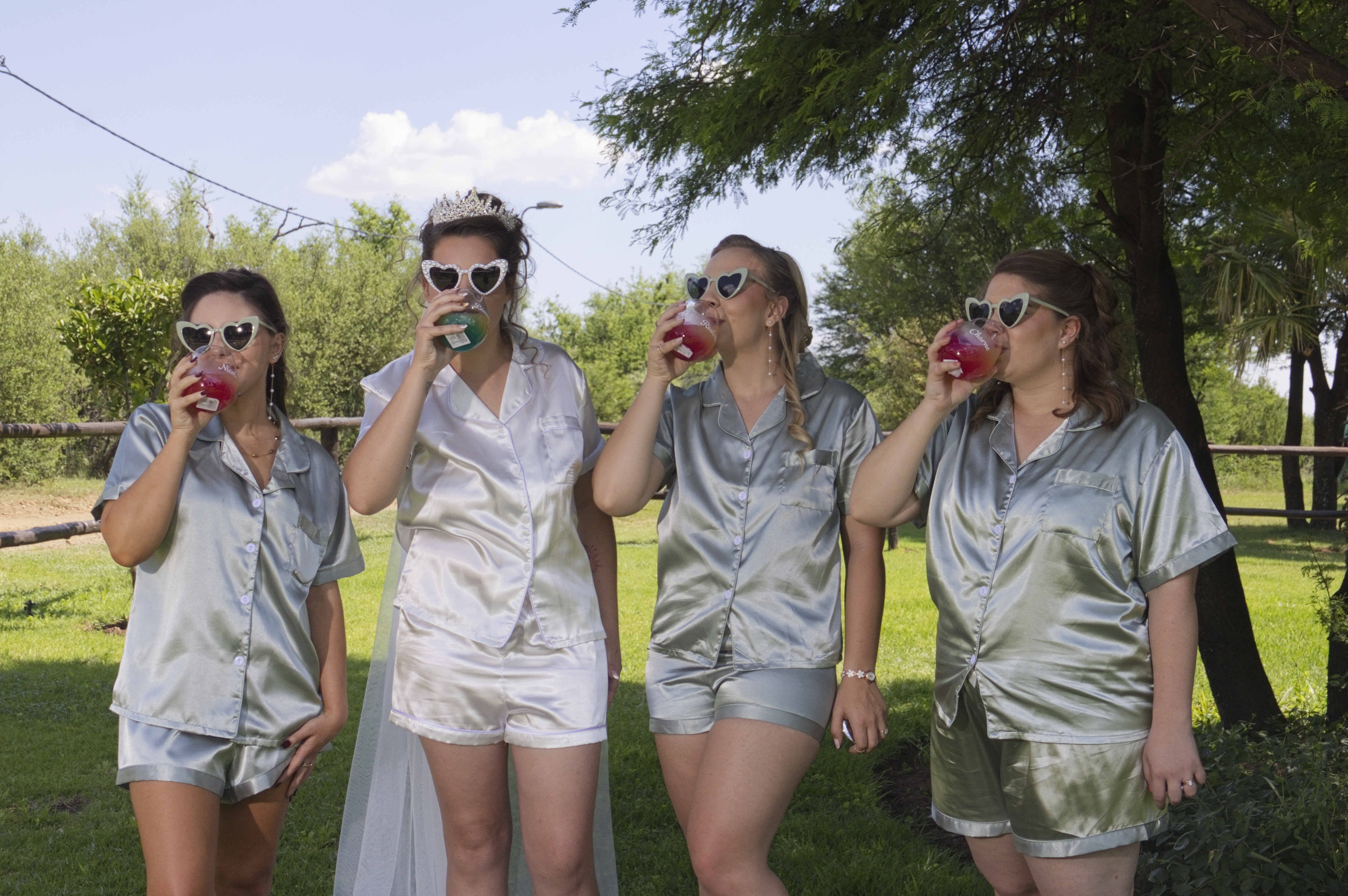 Bride and bridesmaids in satin pyjamas and heart sunglasses sipping cocktails