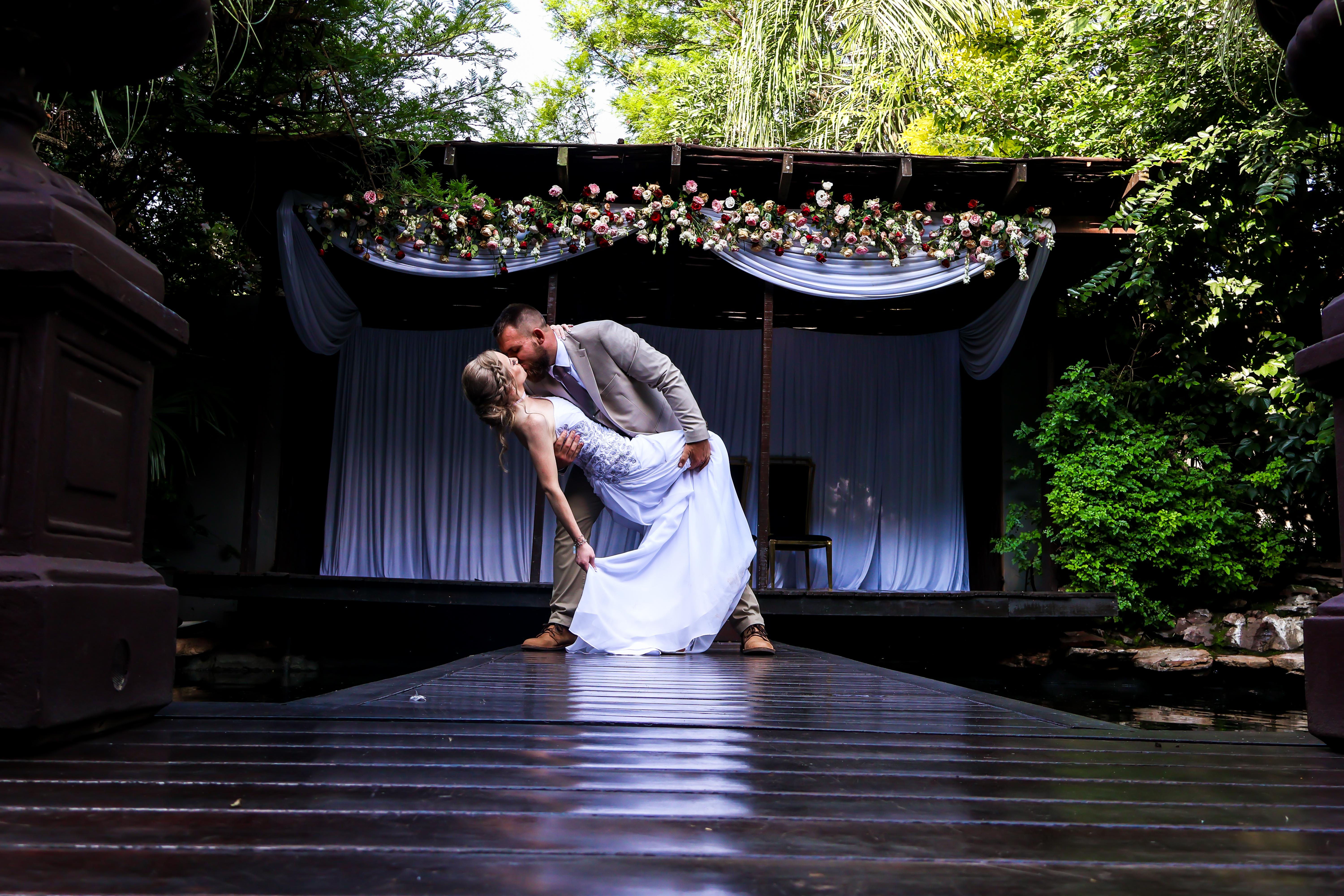 Groom dipping the bride for a kiss before a floral-draped gazebo