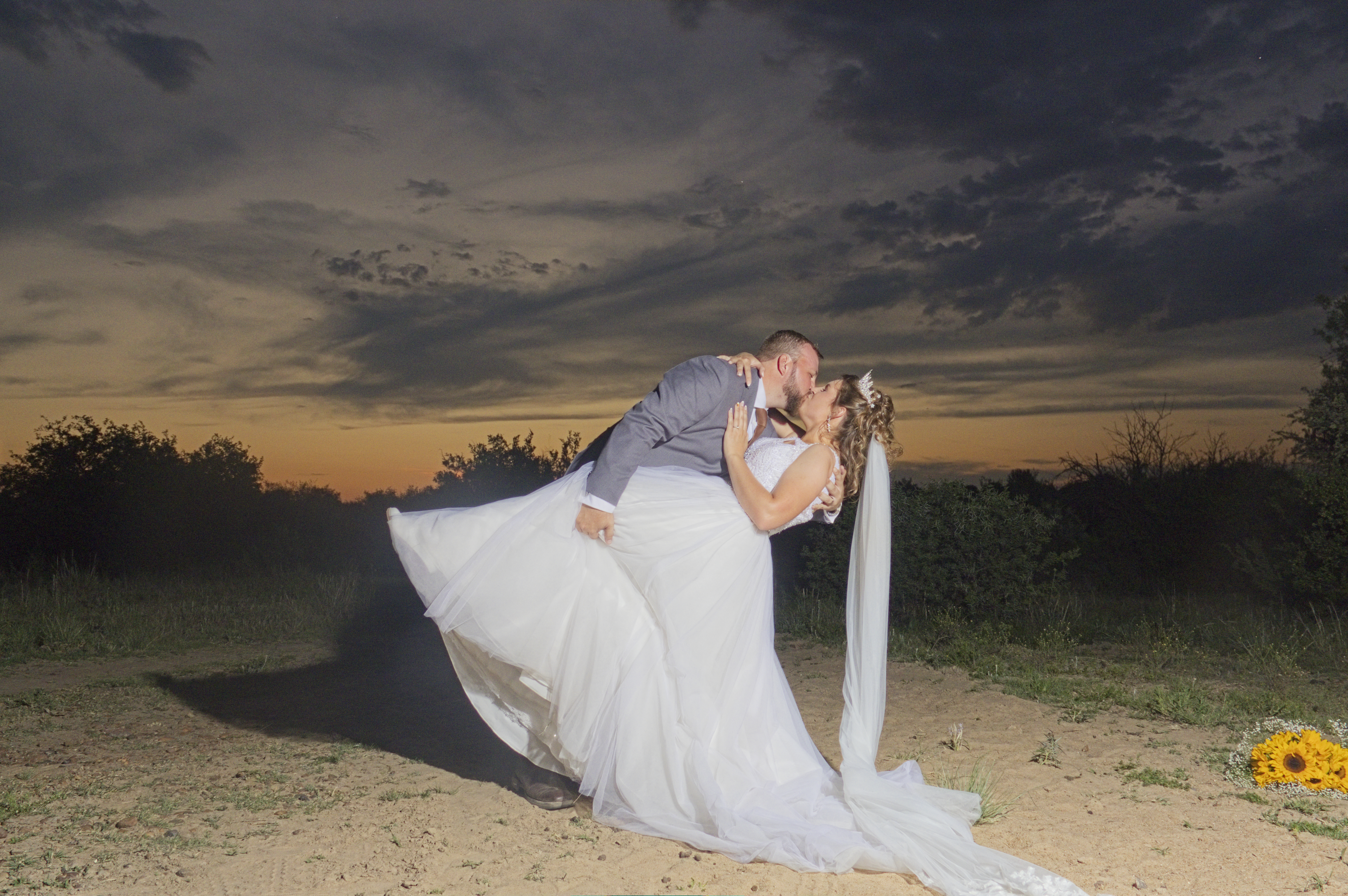 Groom dipping the bride into a kiss under a stormy dusk sky