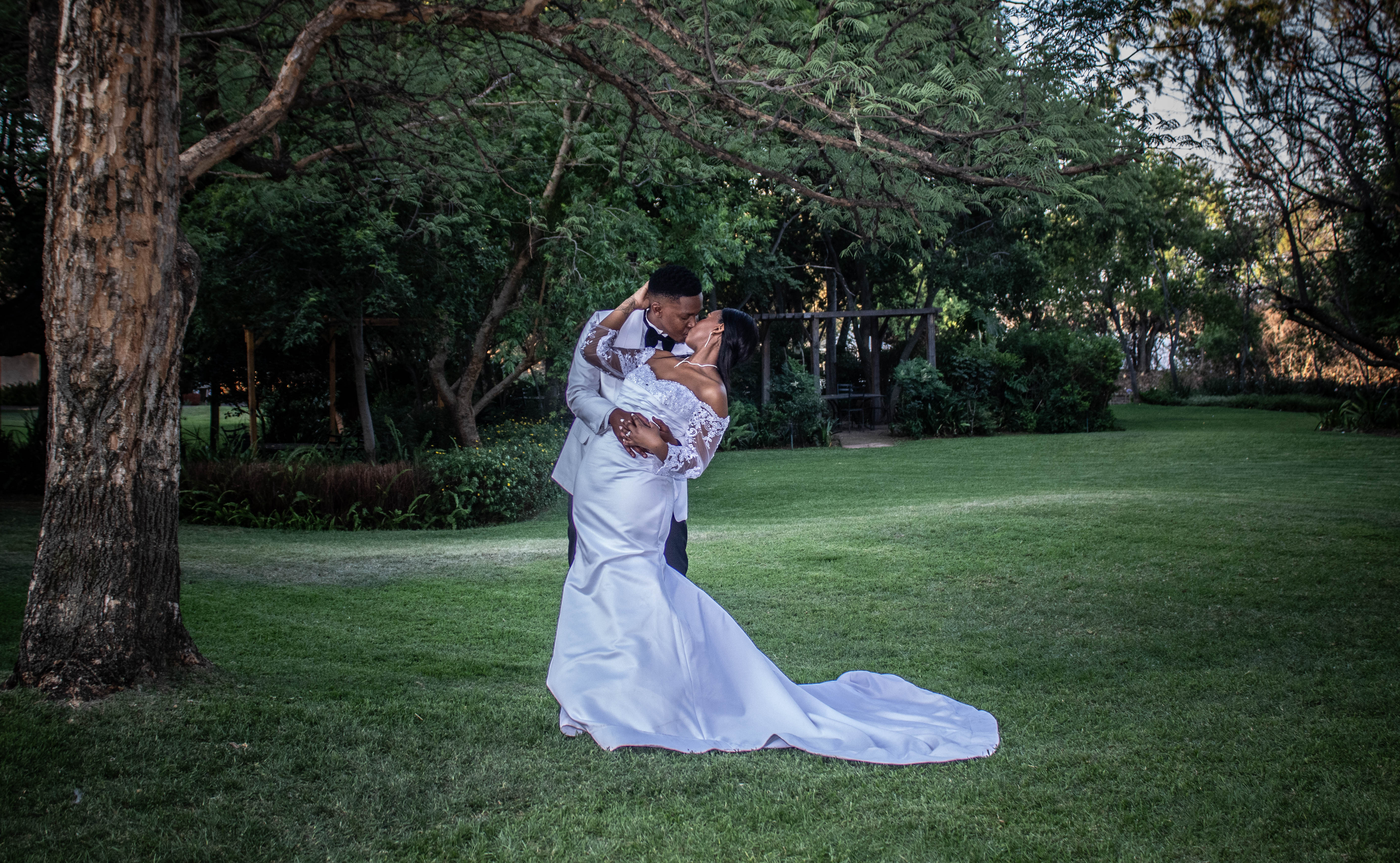 Couple sharing a dip kiss beneath a sprawling garden tree