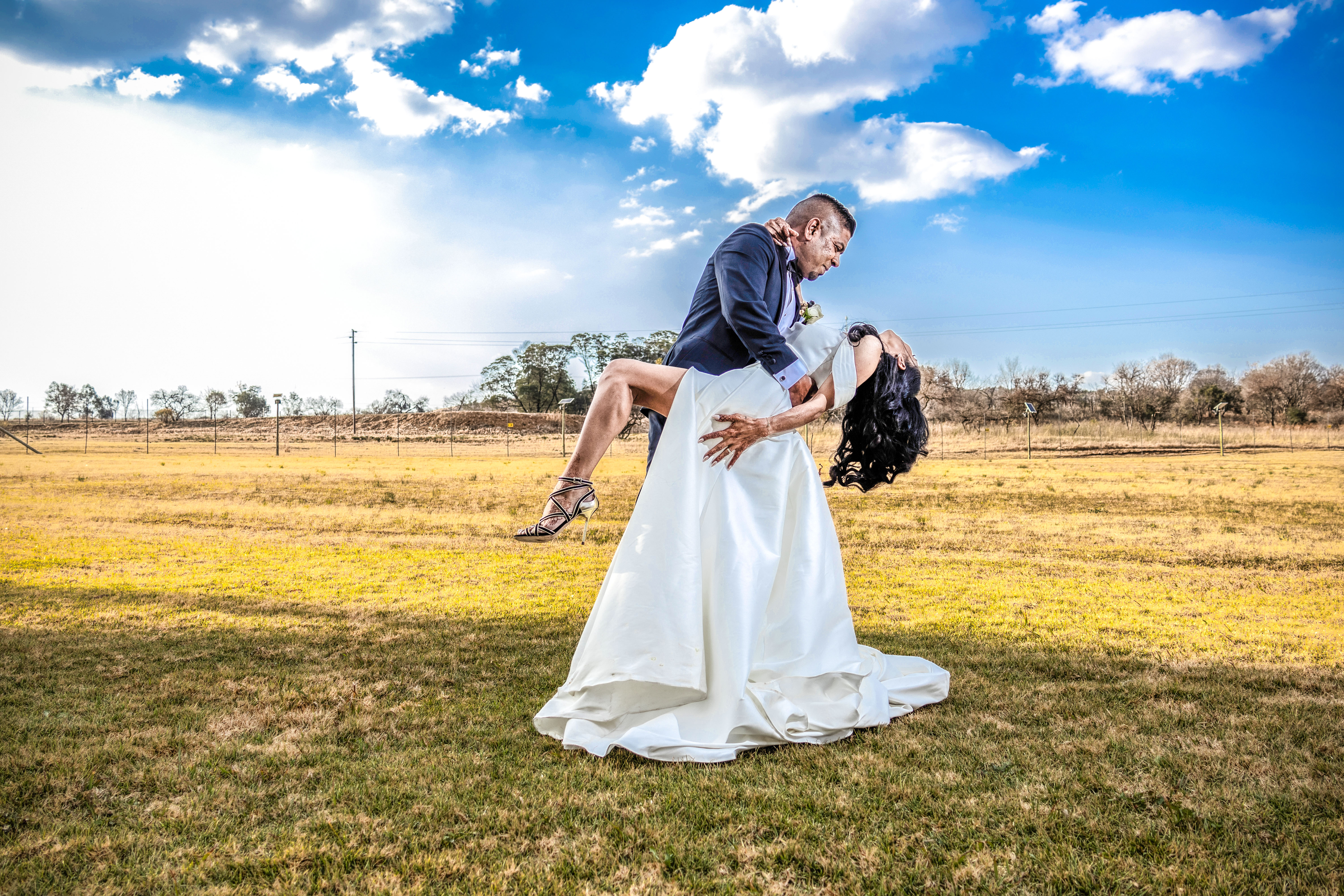 Groom dramatically dipping the bride in a field under a blue sky