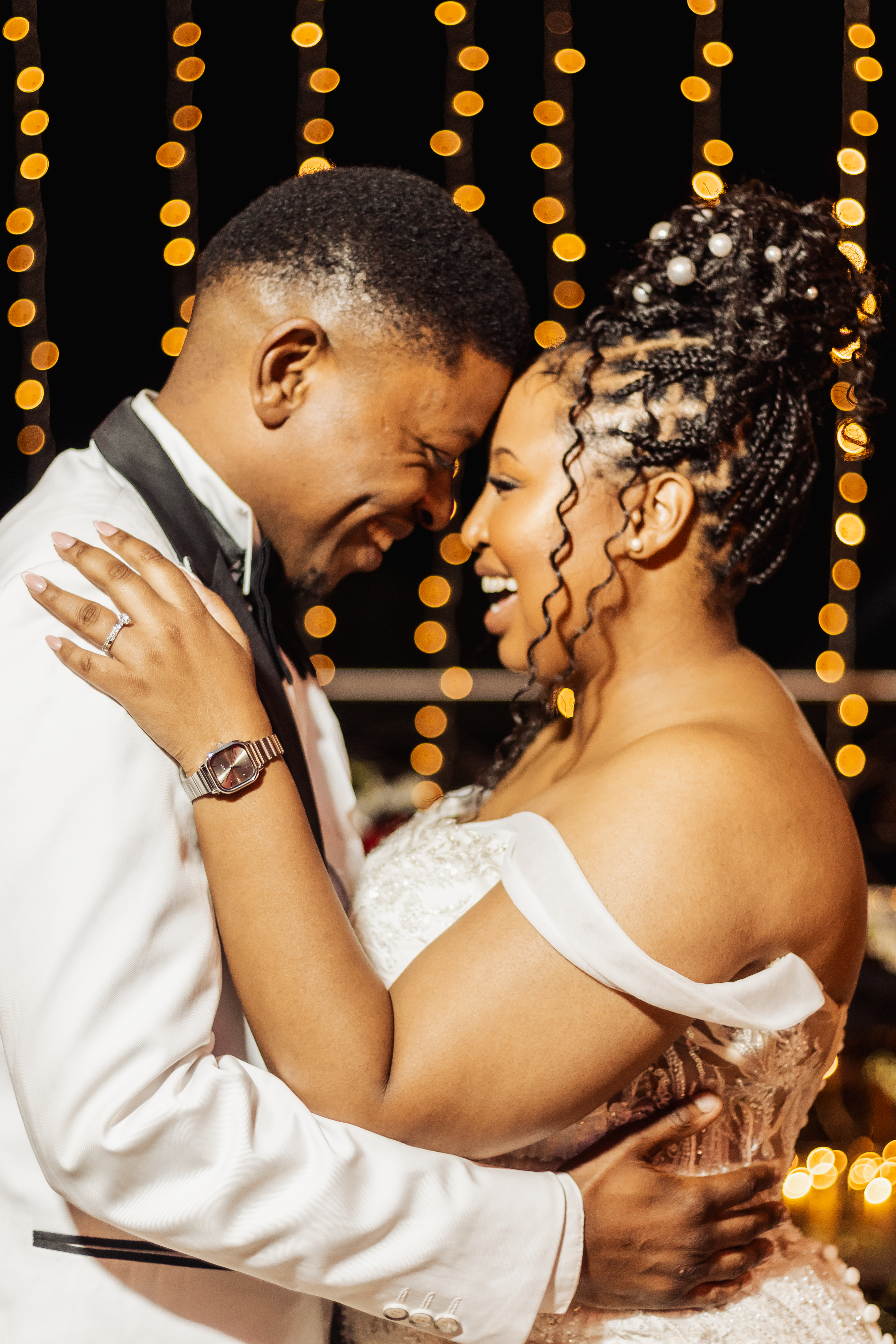 Couple sharing a tender first dance beneath golden string lights