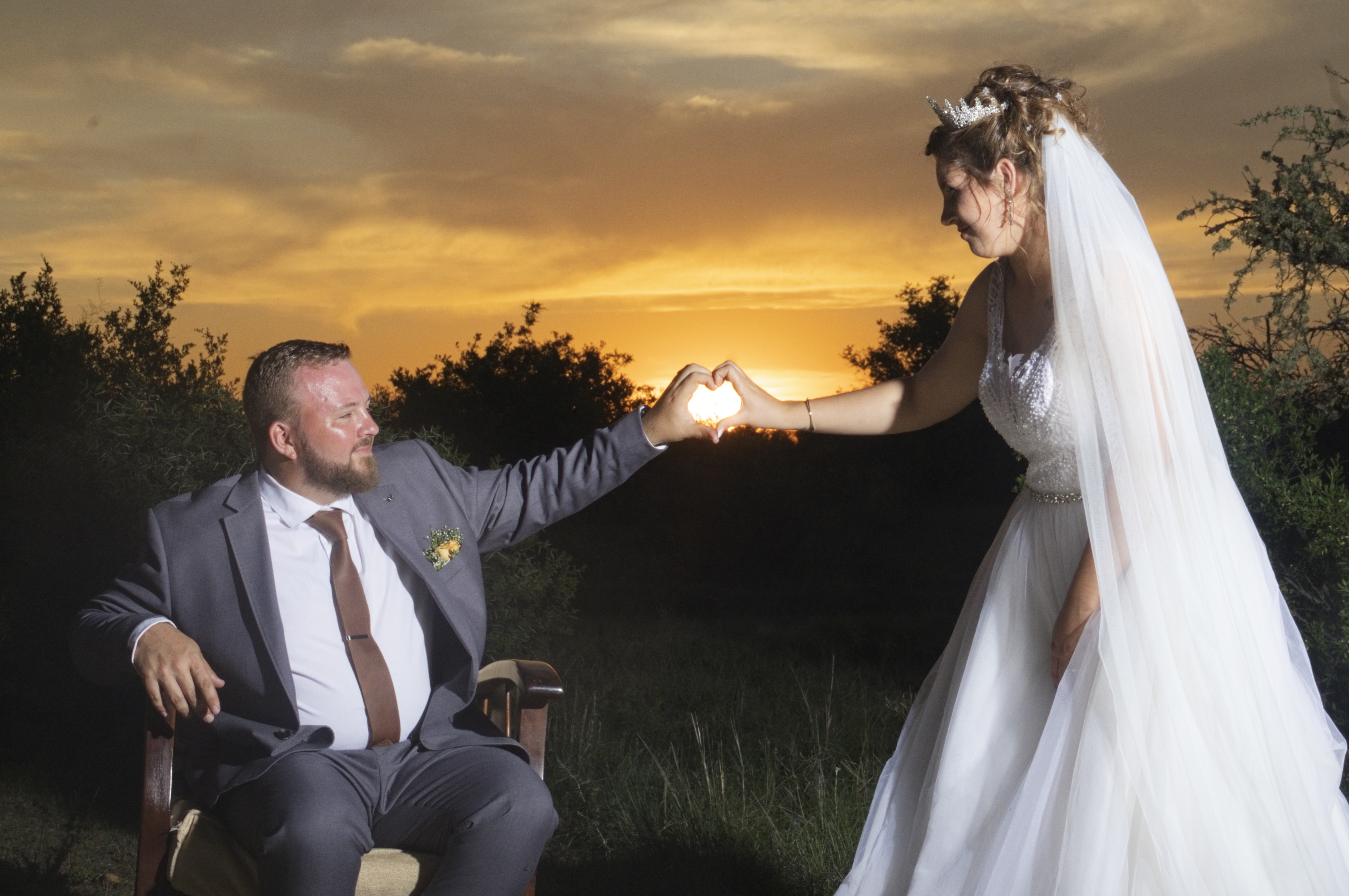 Couple forming a heart with their hands around the setting sun