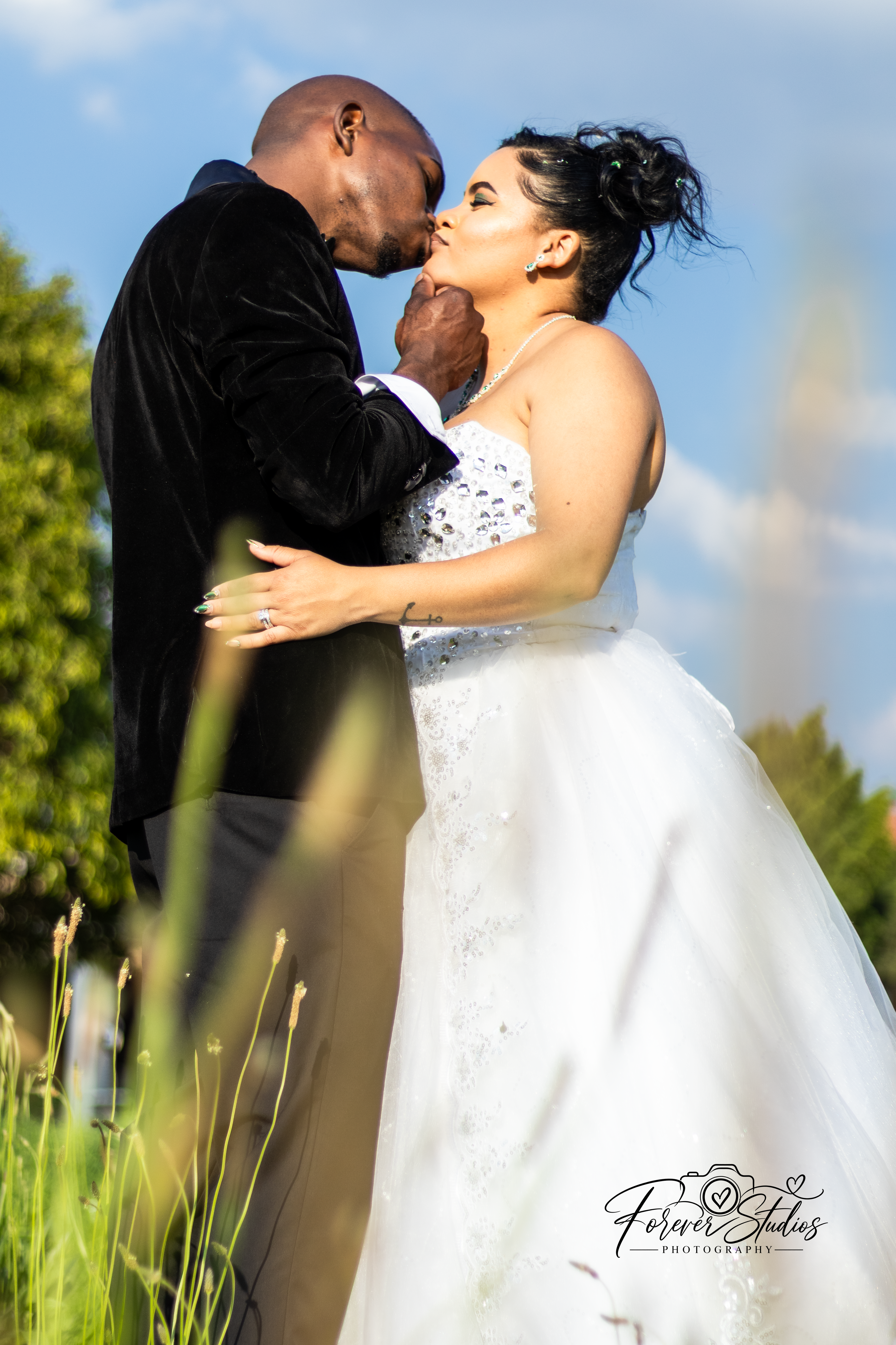 Bride and groom kissing against a blue sky