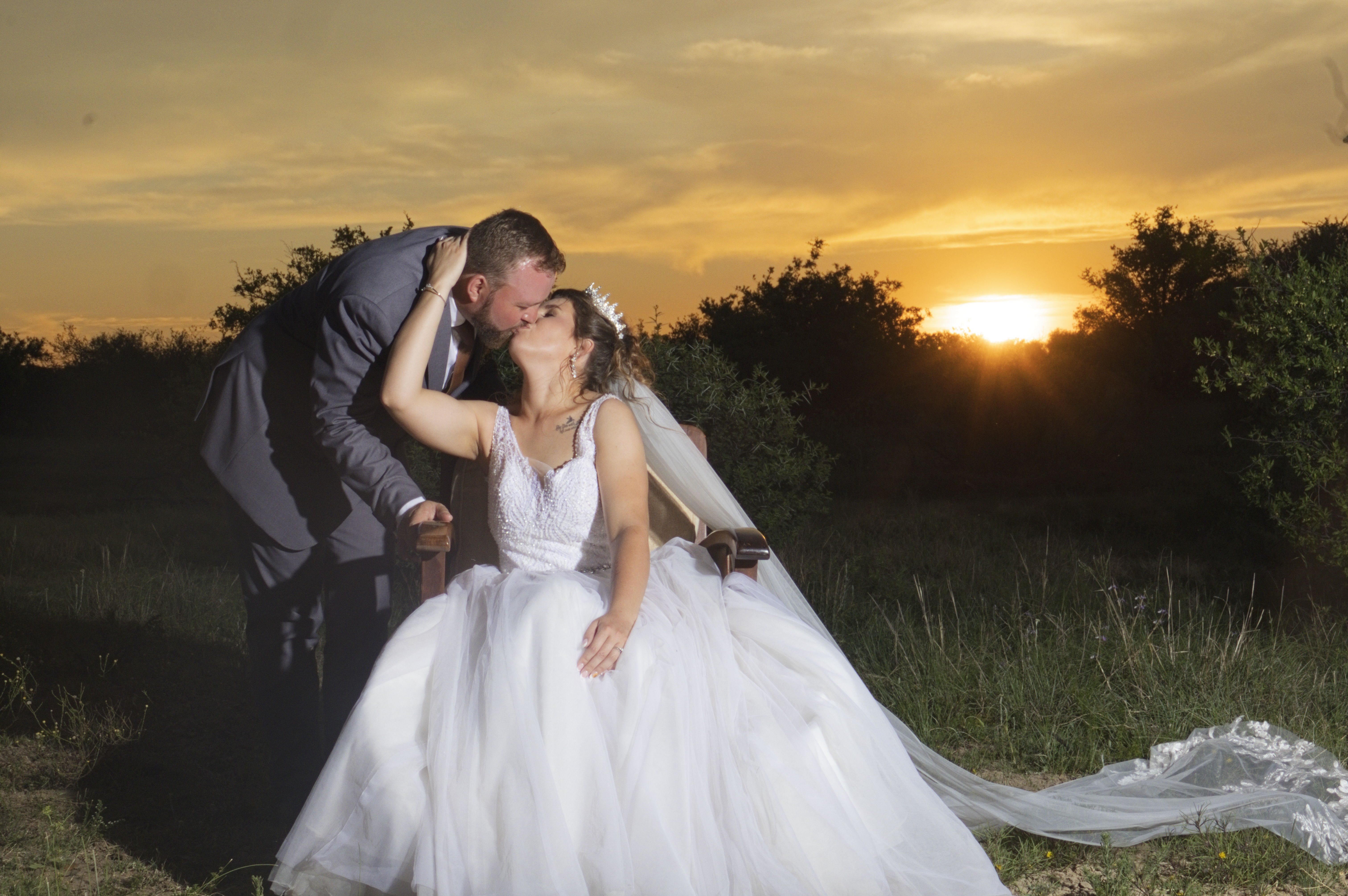 Groom kissing the seated bride against a golden sunset
