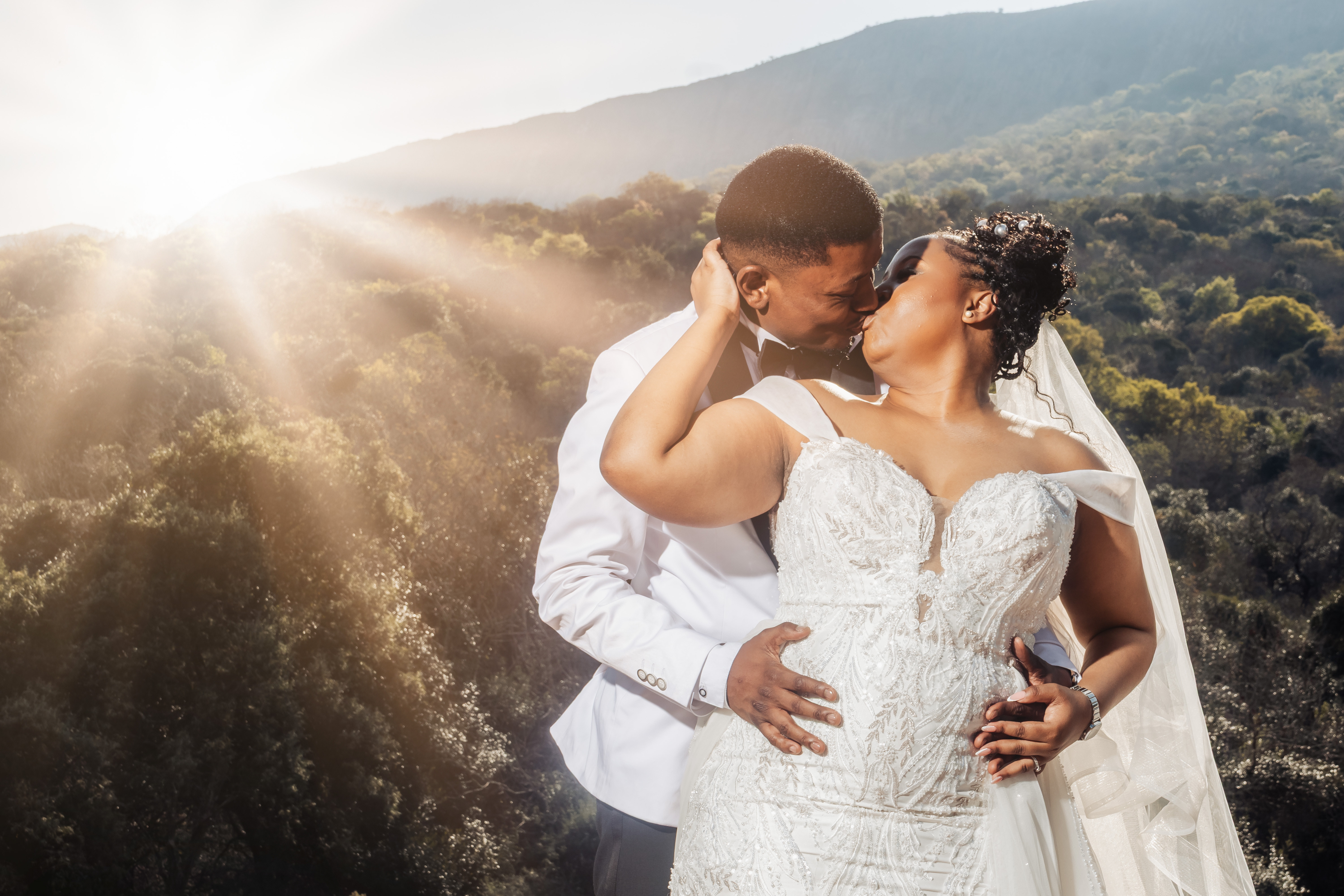 Couple kissing against a mountain backdrop with golden sun rays