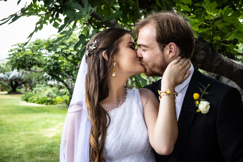 Bride and groom kissing beneath a leafy fig tree