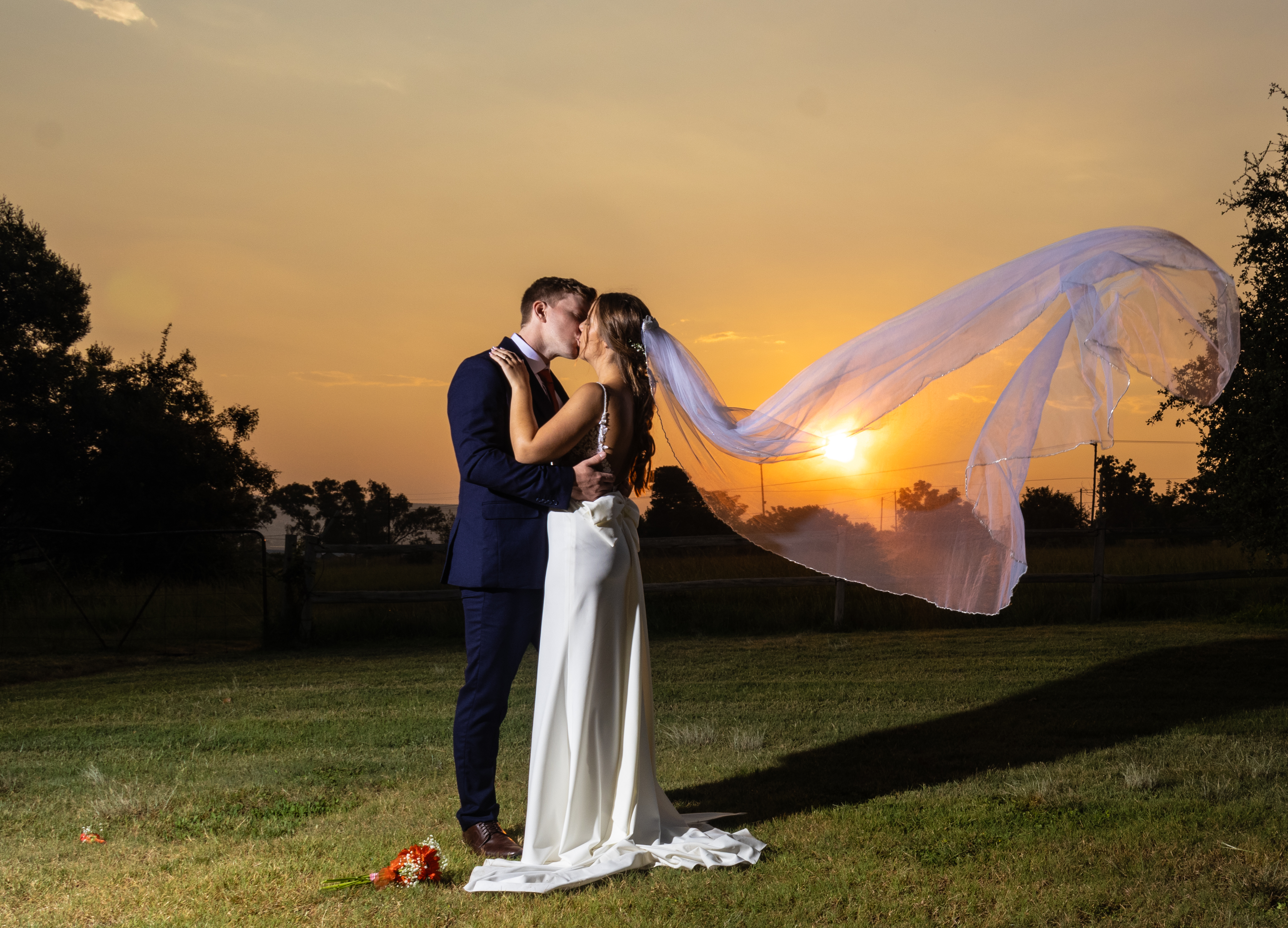 Couple kissing at sunset with the bride's veil flying in the breeze