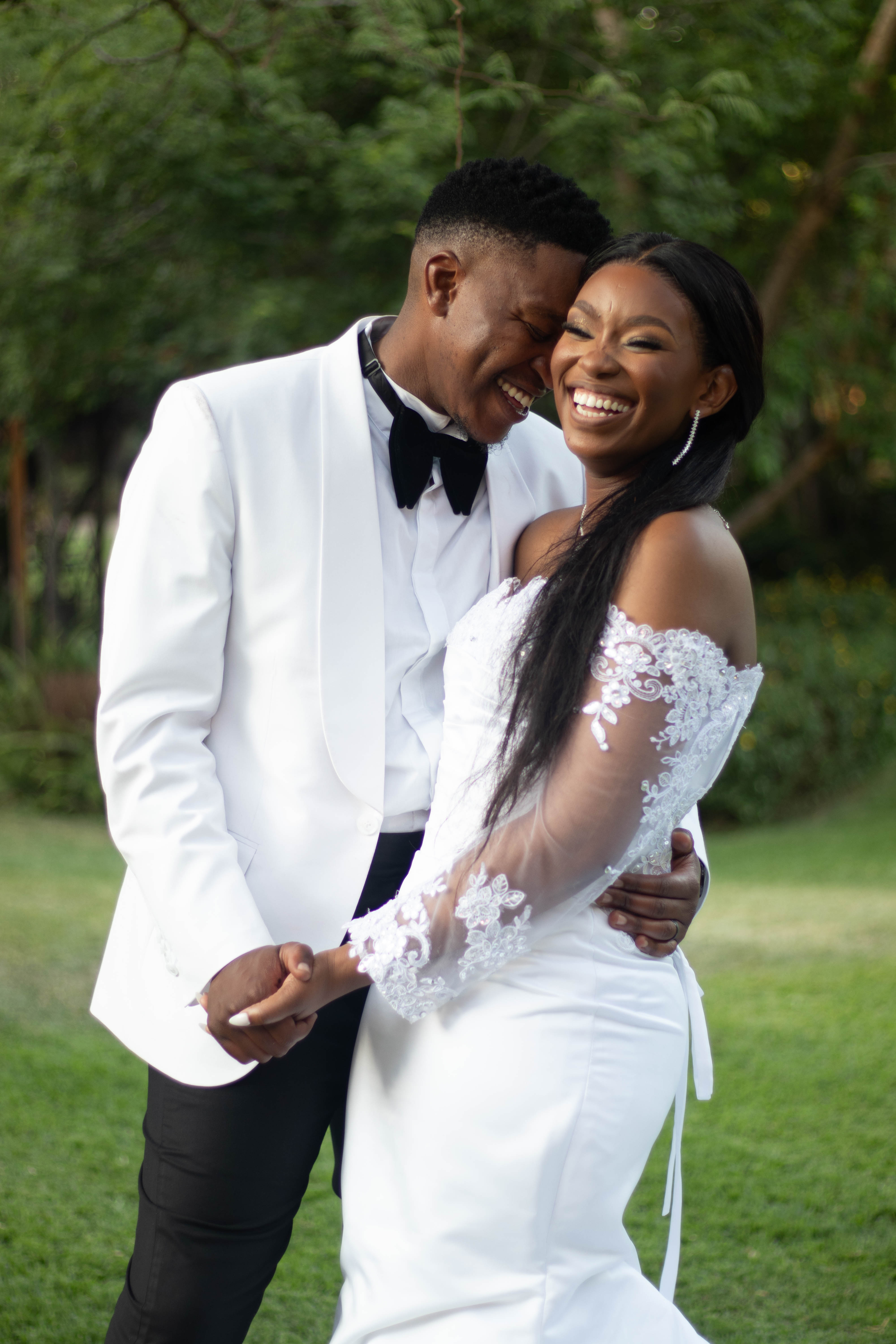 Laughing bride and groom in a white tuxedo on a garden lawn