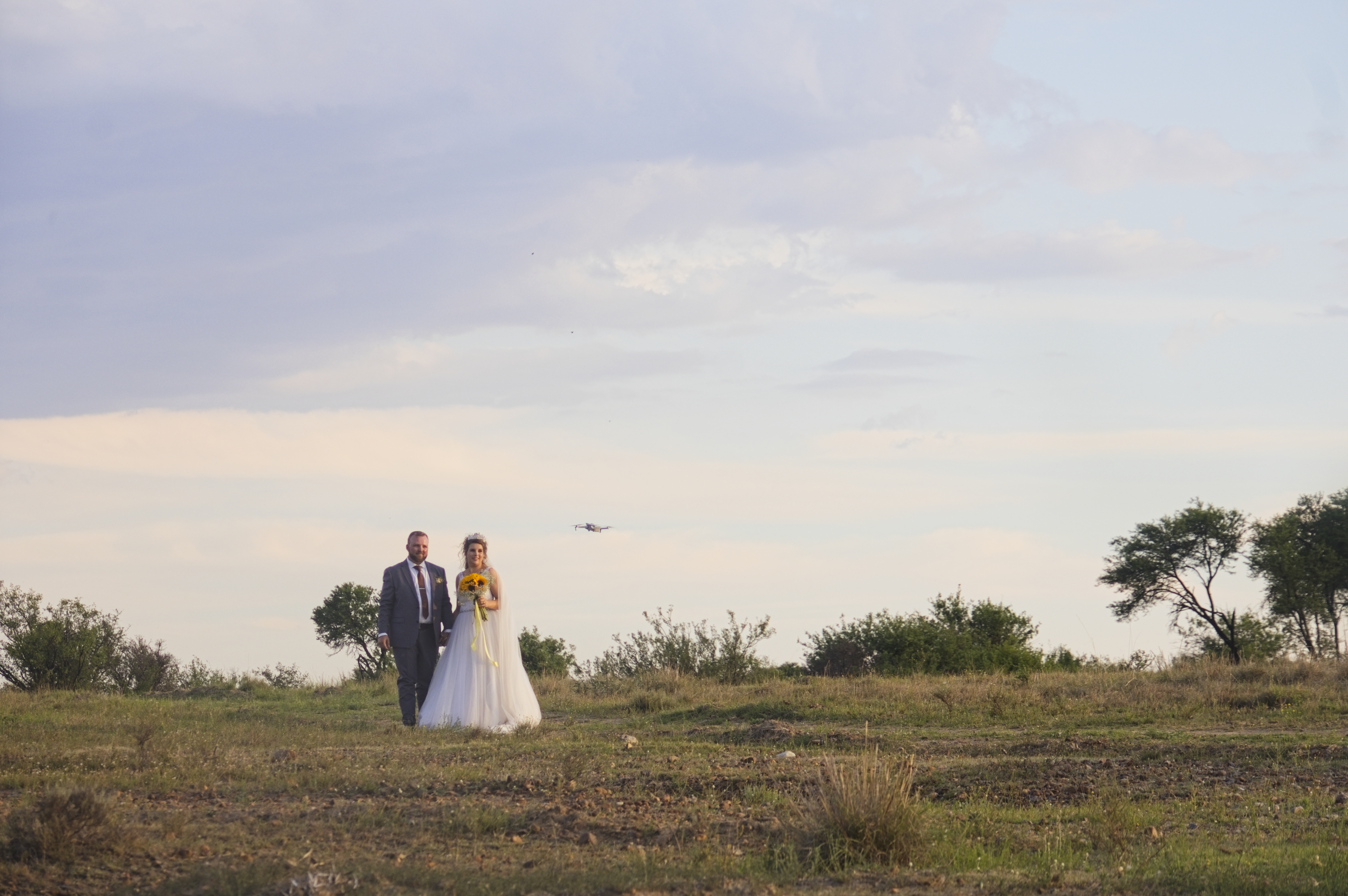 Couple in an open bushveld field with a drone capturing the moment