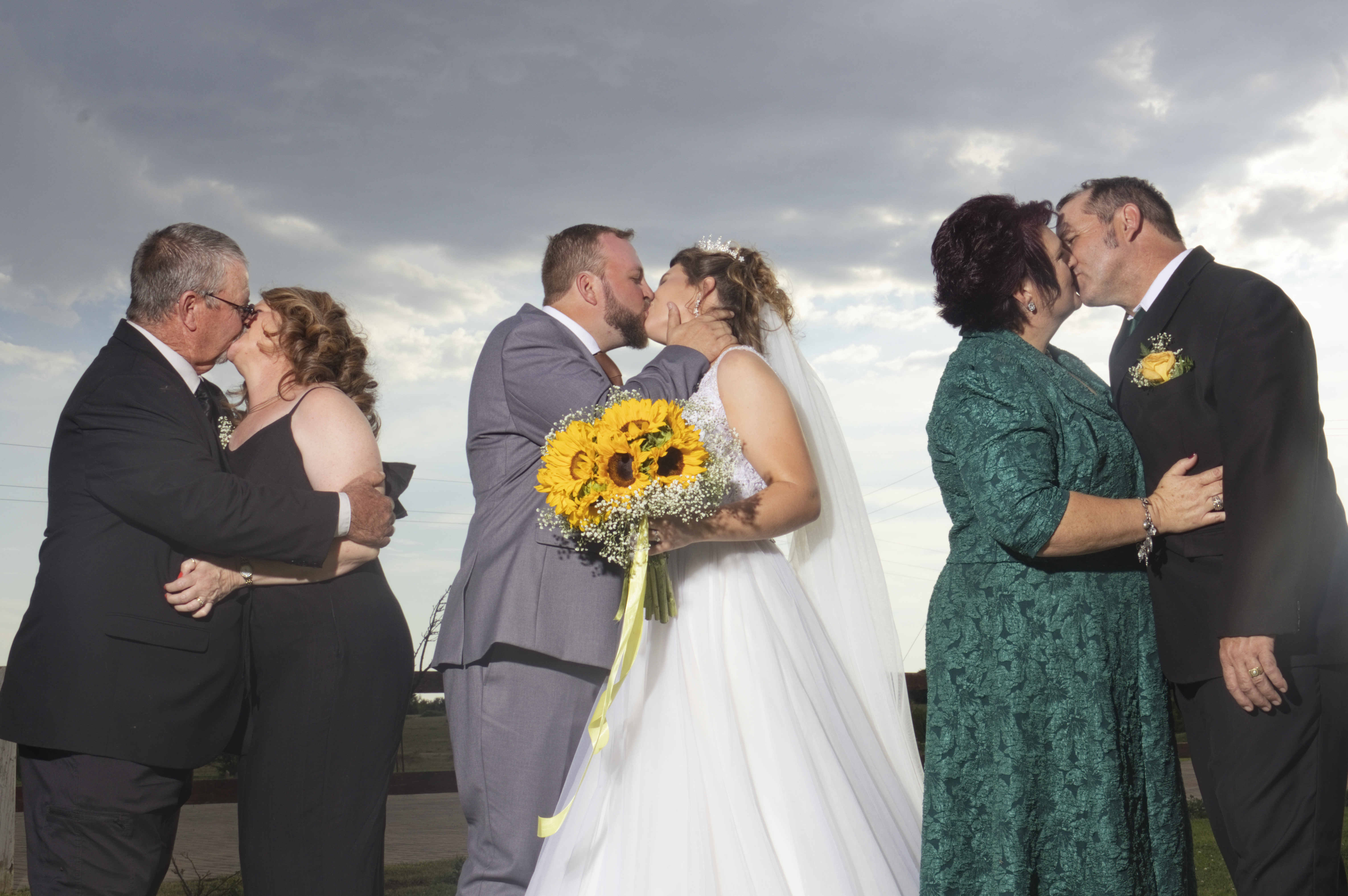 Bride, groom and both sets of parents sharing a kiss