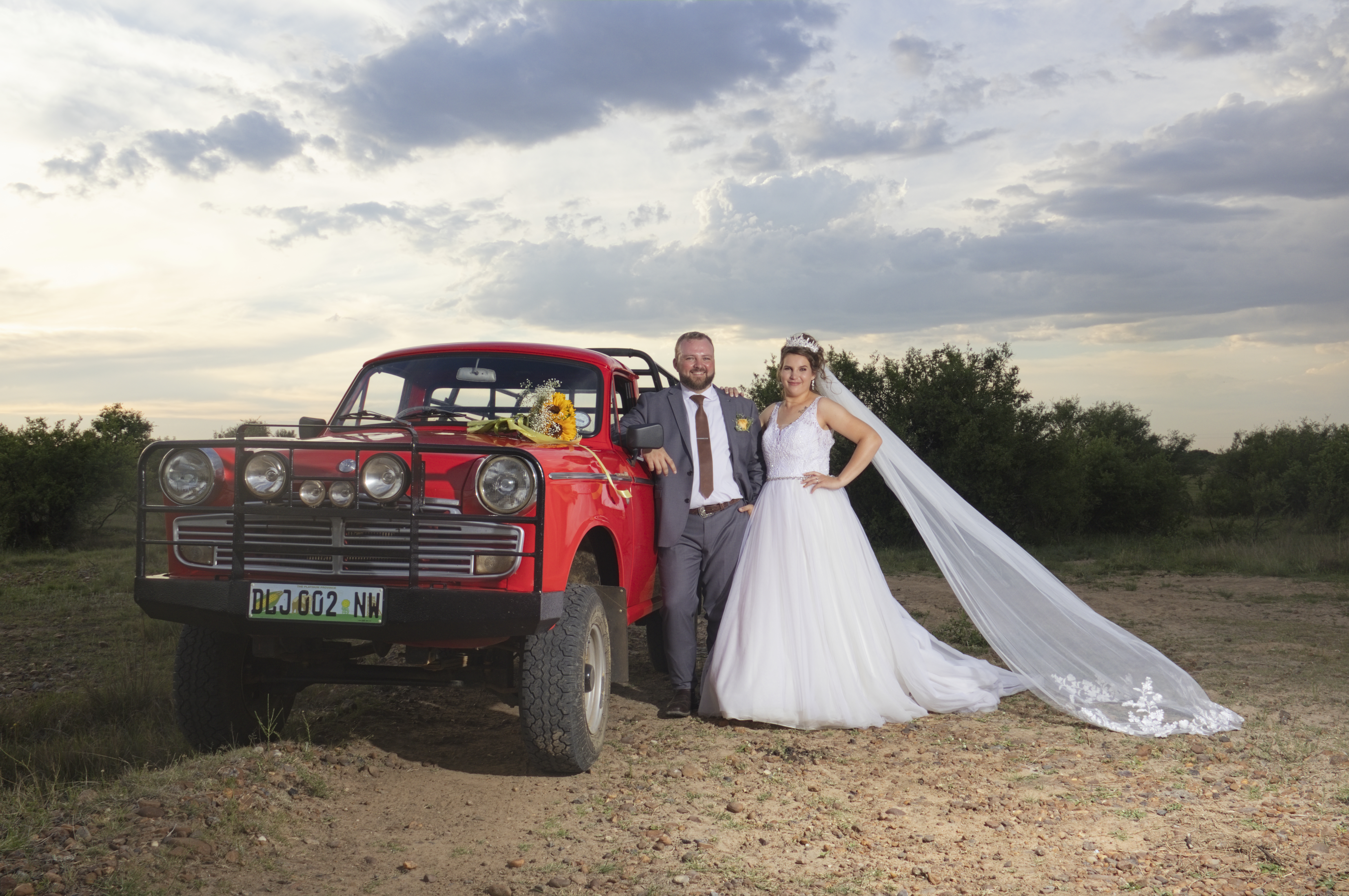Couple beside a vintage red Datsun with the veil flowing in the wind