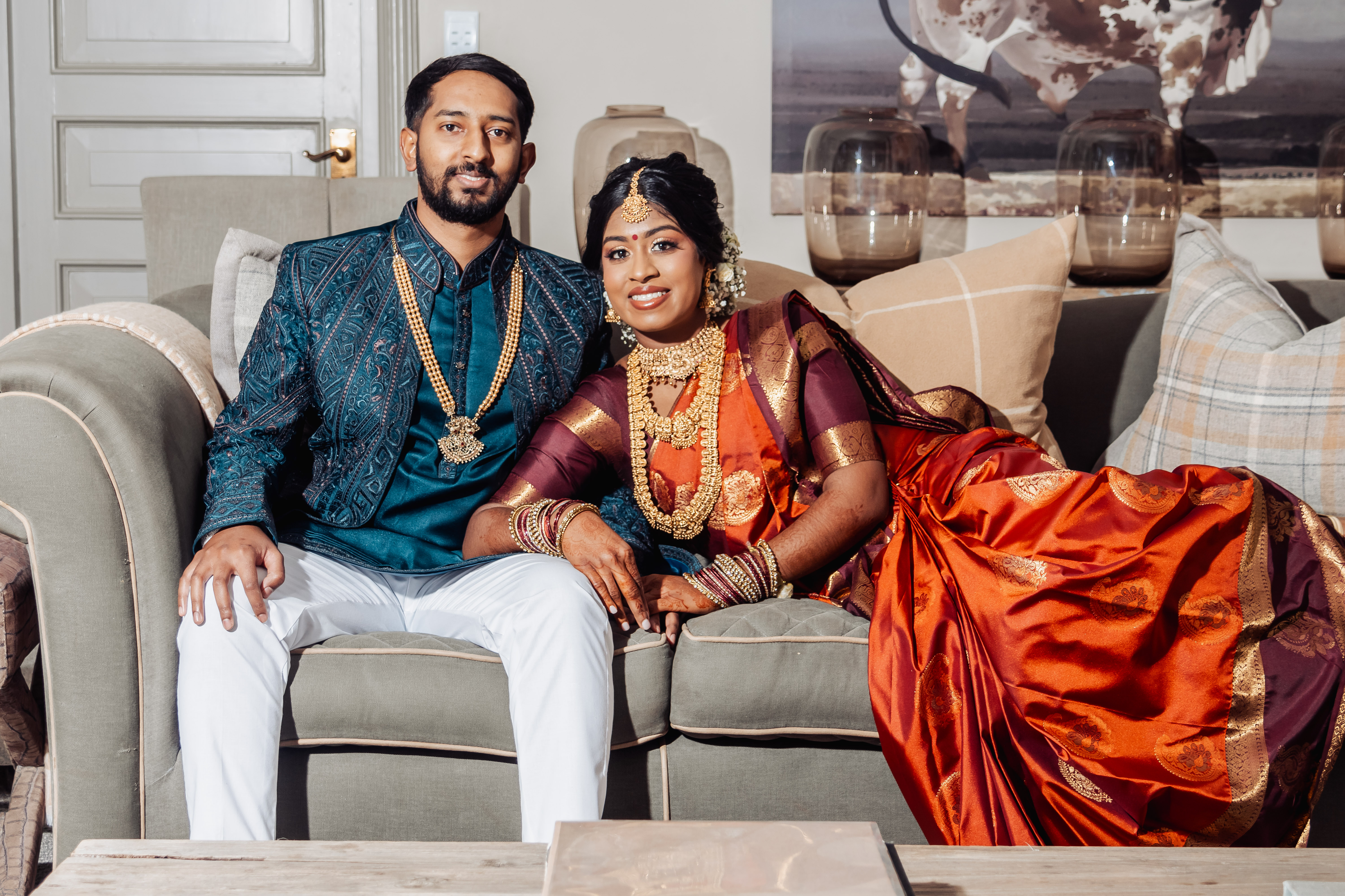 Couple in traditional wedding attire and gold jewellery seated on a sofa