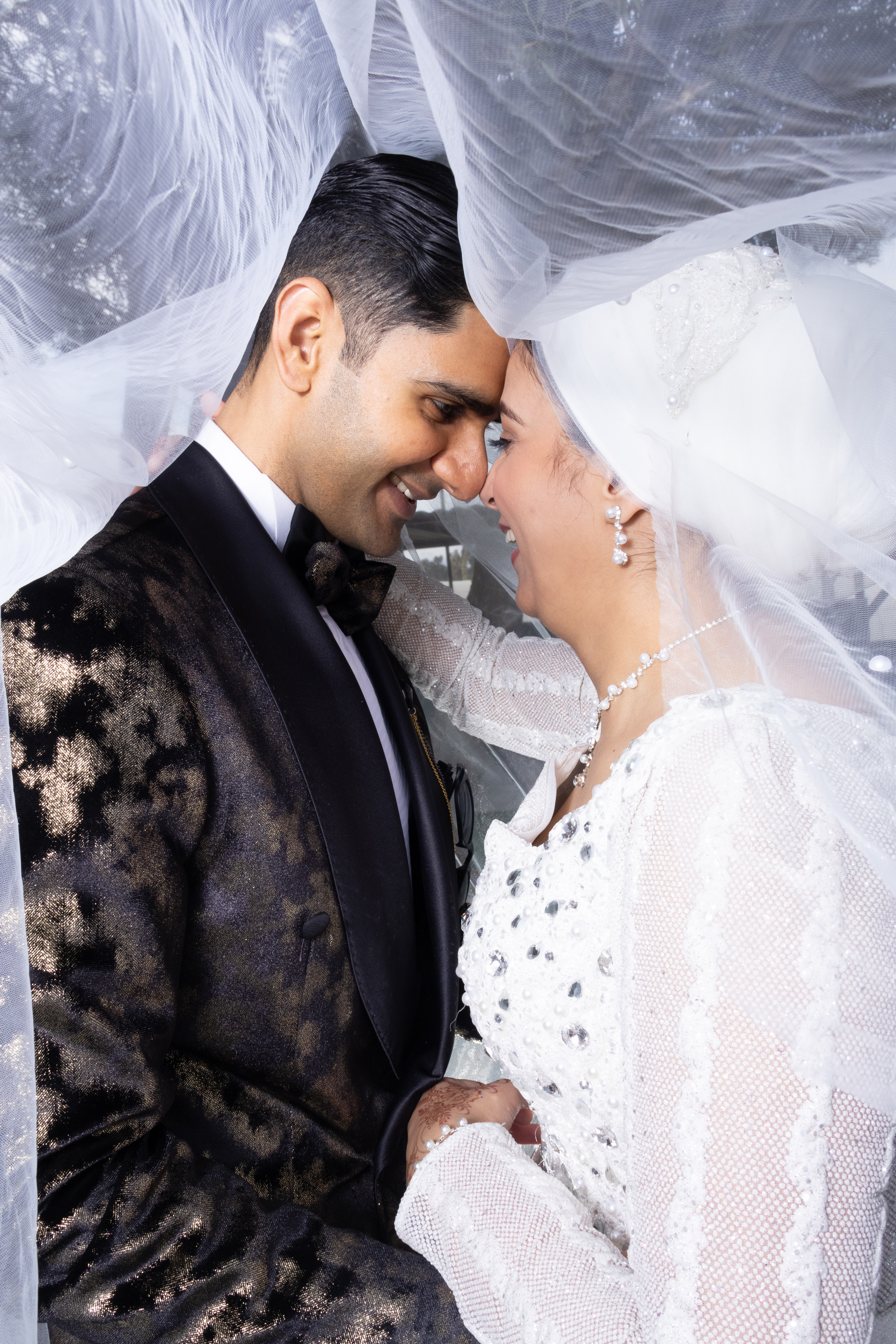Couple touching foreheads and smiling beneath a sheer veil
