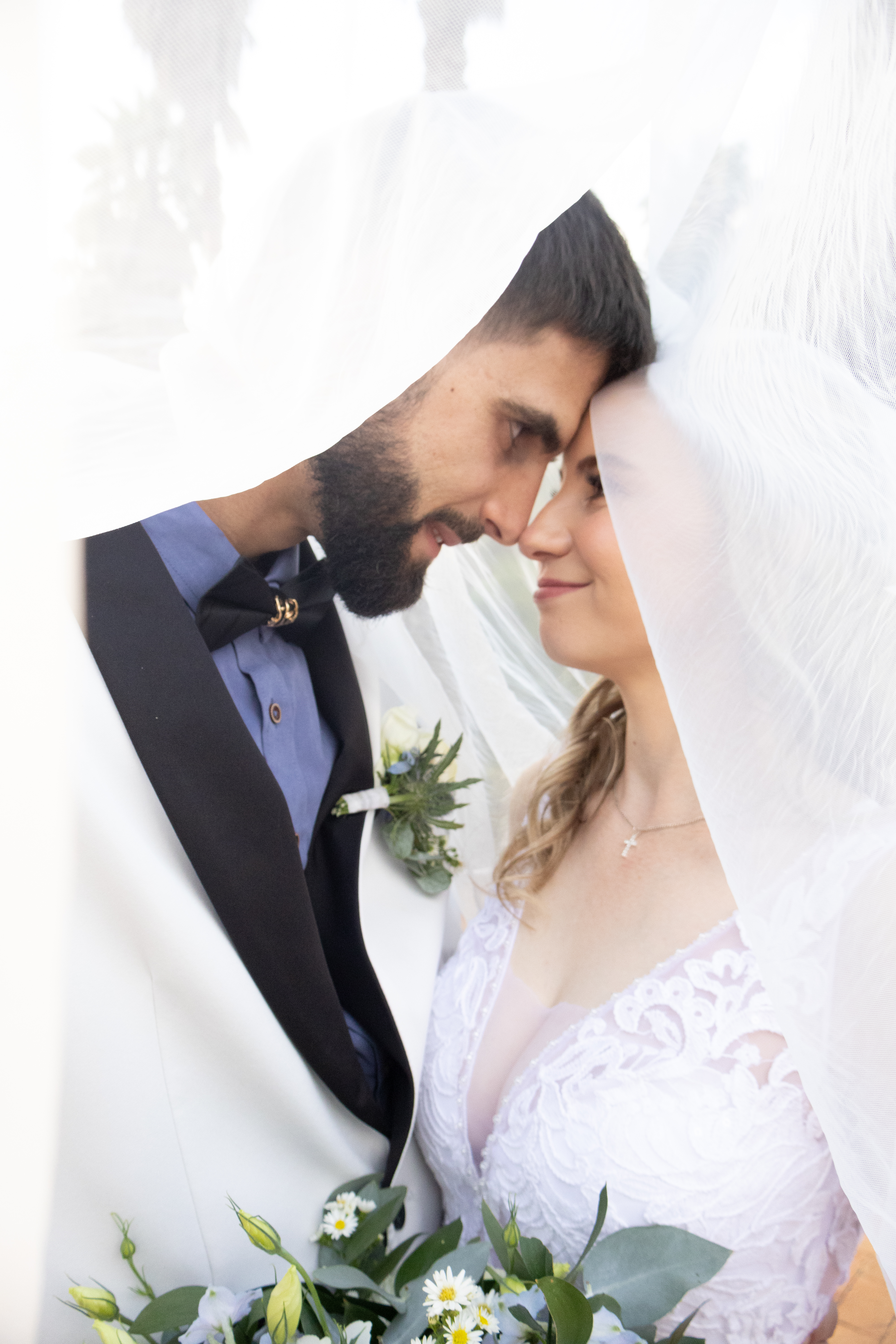 Couple touching foreheads beneath a veil with a daisy bouquet