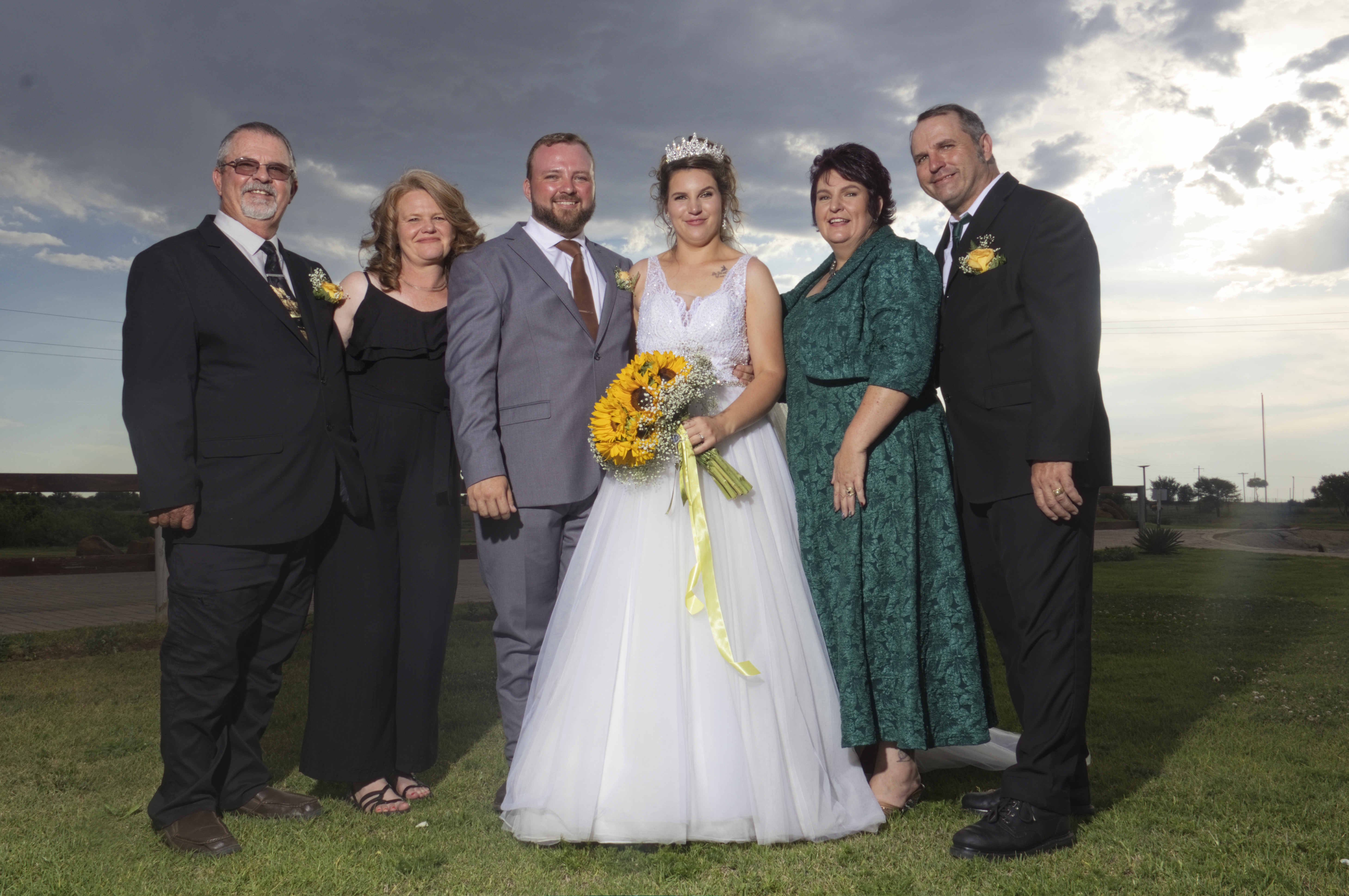 Bride and groom with their parents under a dramatic sky