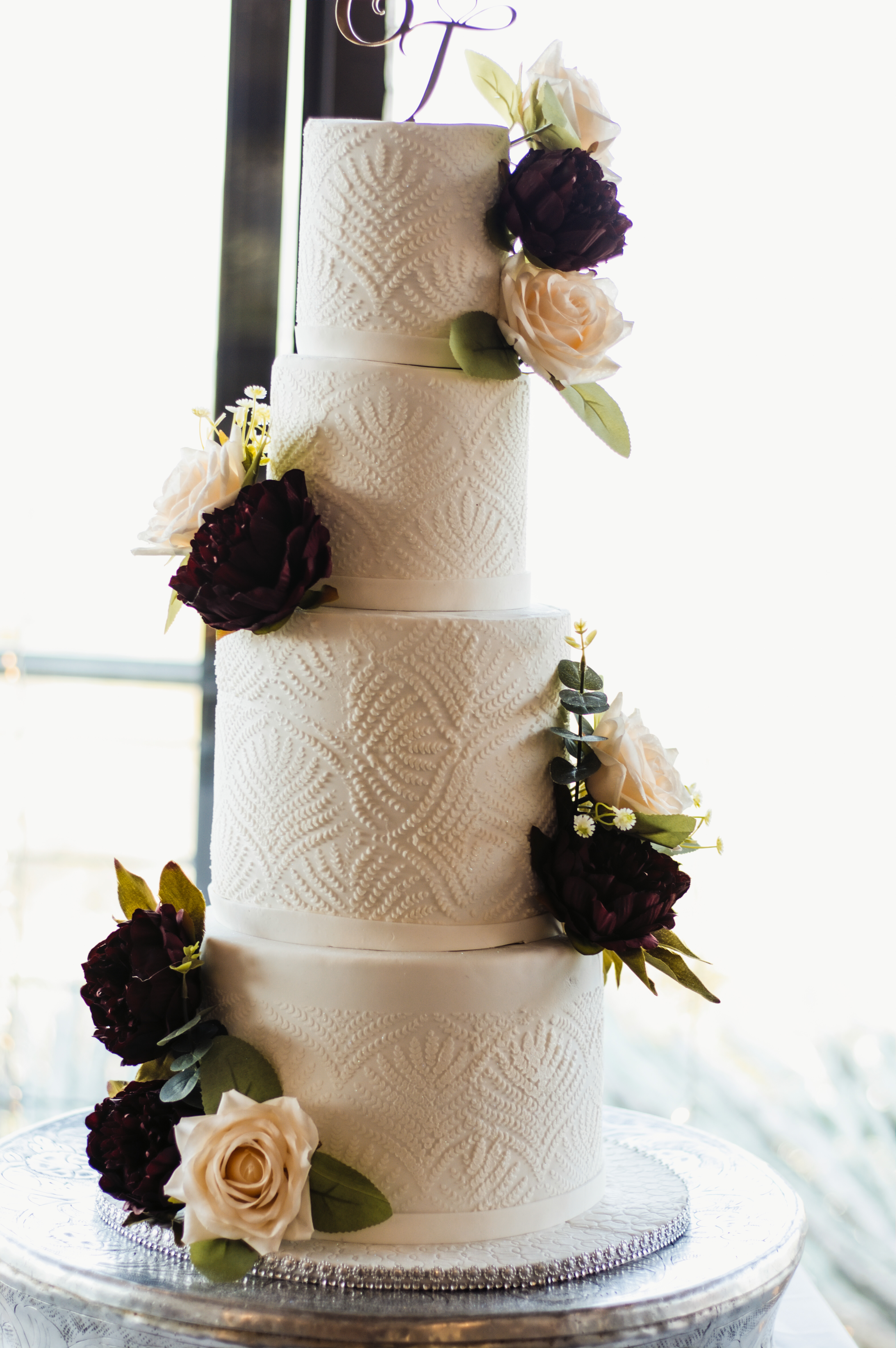 Four-tier white wedding cake with burgundy peonies and ivory roses