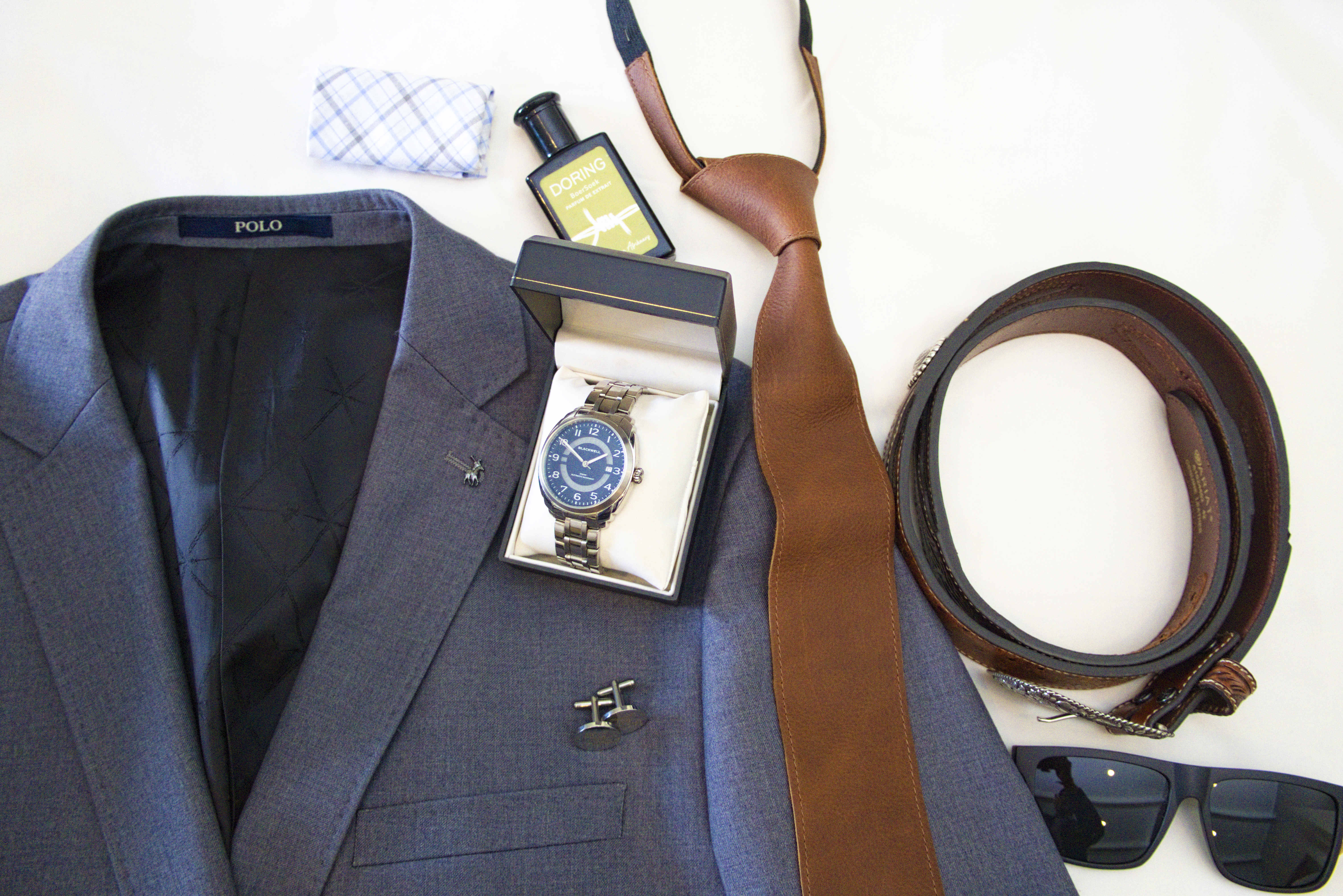 Flat lay of the groom's suit, watch, leather tie, belt and accessories