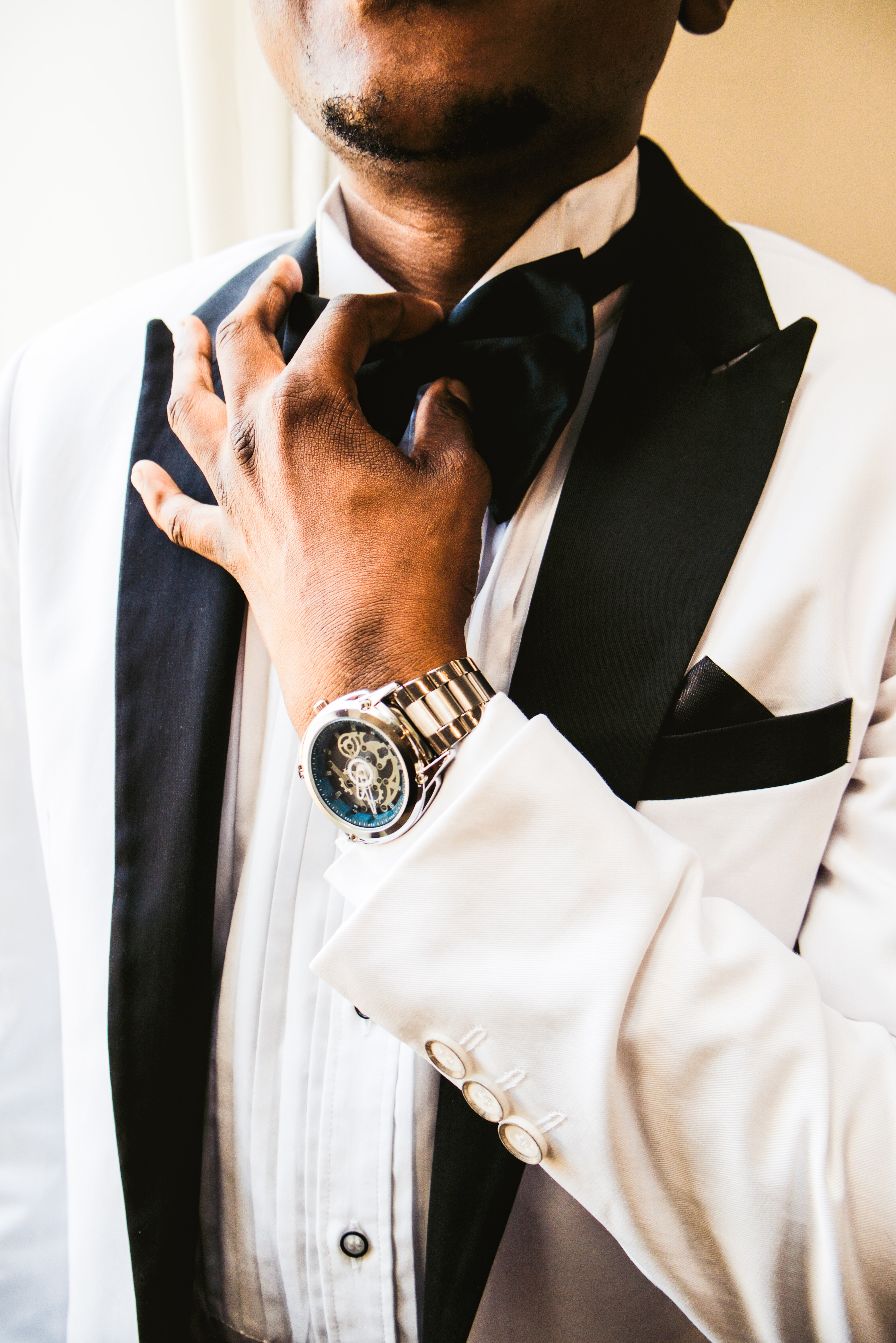 Close-up of the groom adjusting his bow tie, wearing a skeleton watch