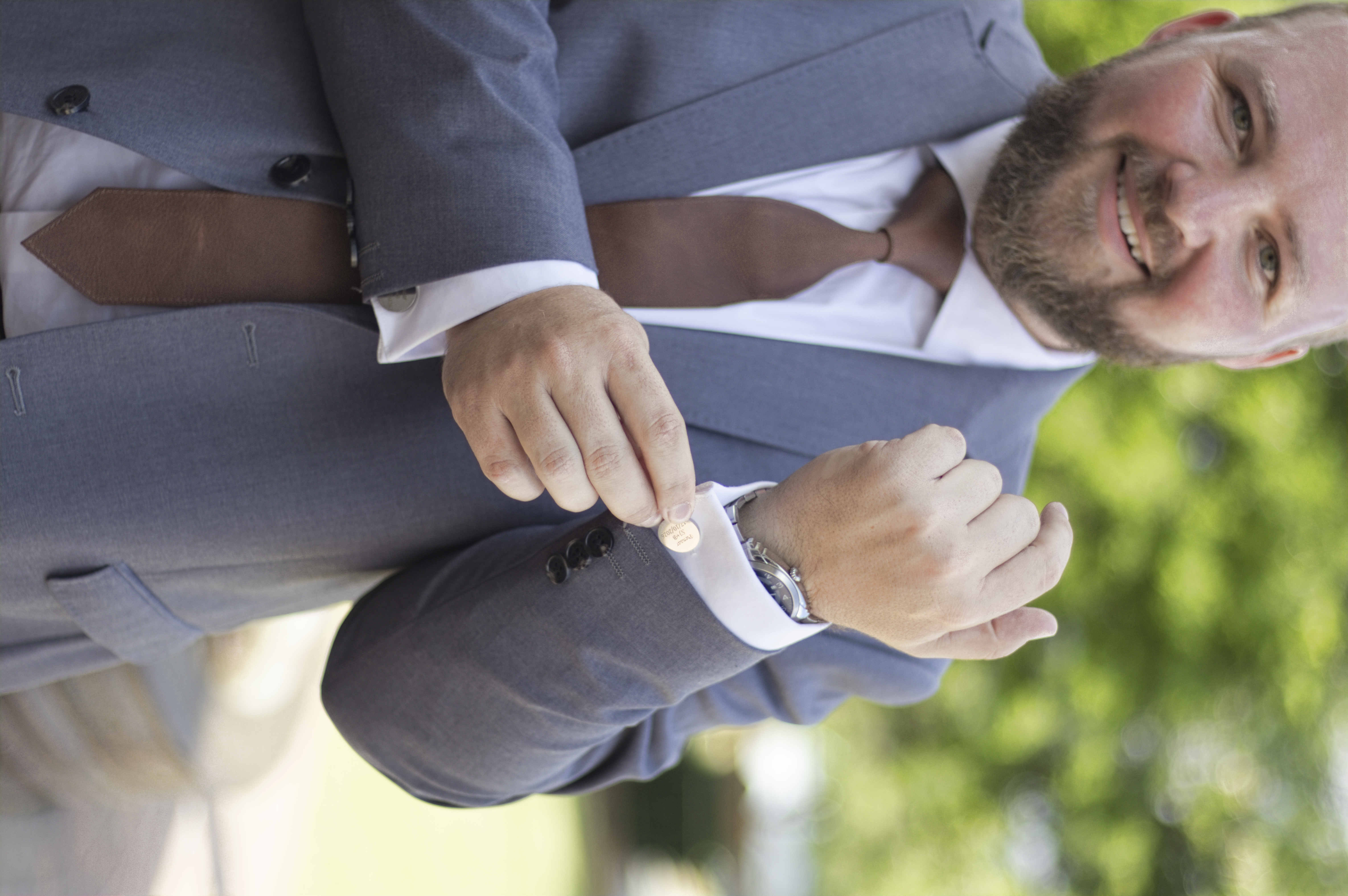 Smiling groom fastening an engraved cufflink