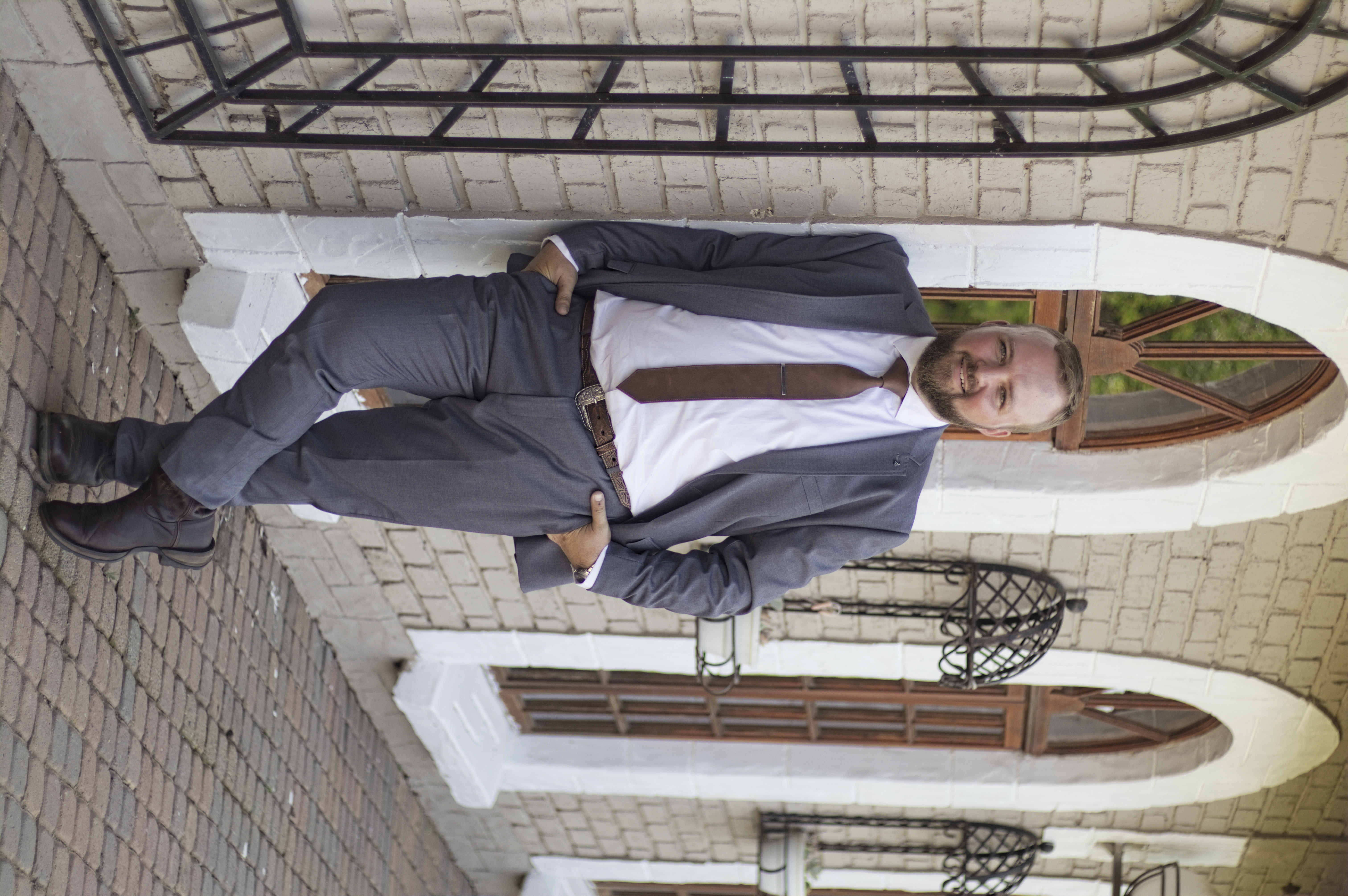 Groom leaning against an arched window in a grey suit