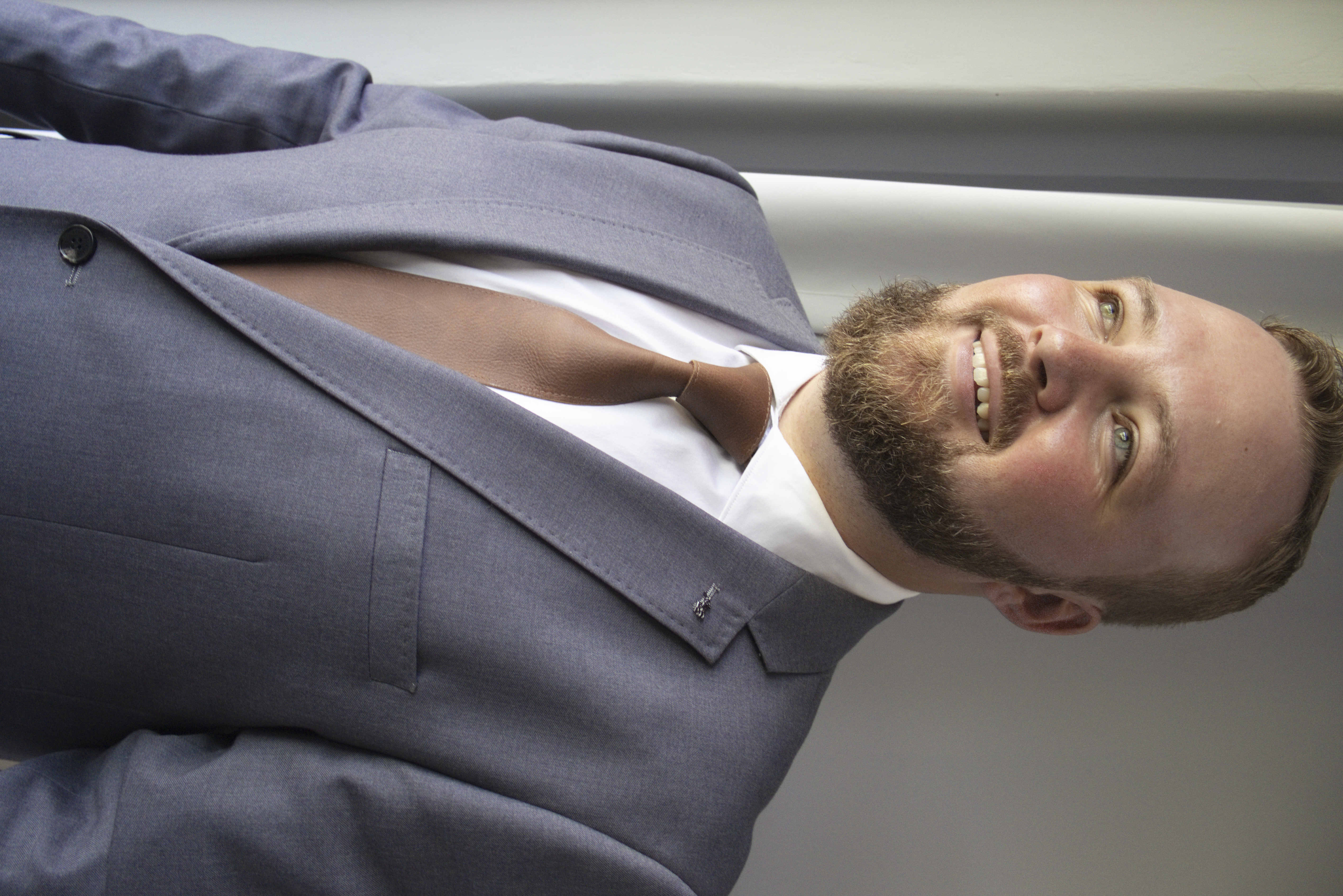 Smiling groom in a grey suit and leather tie by the window
