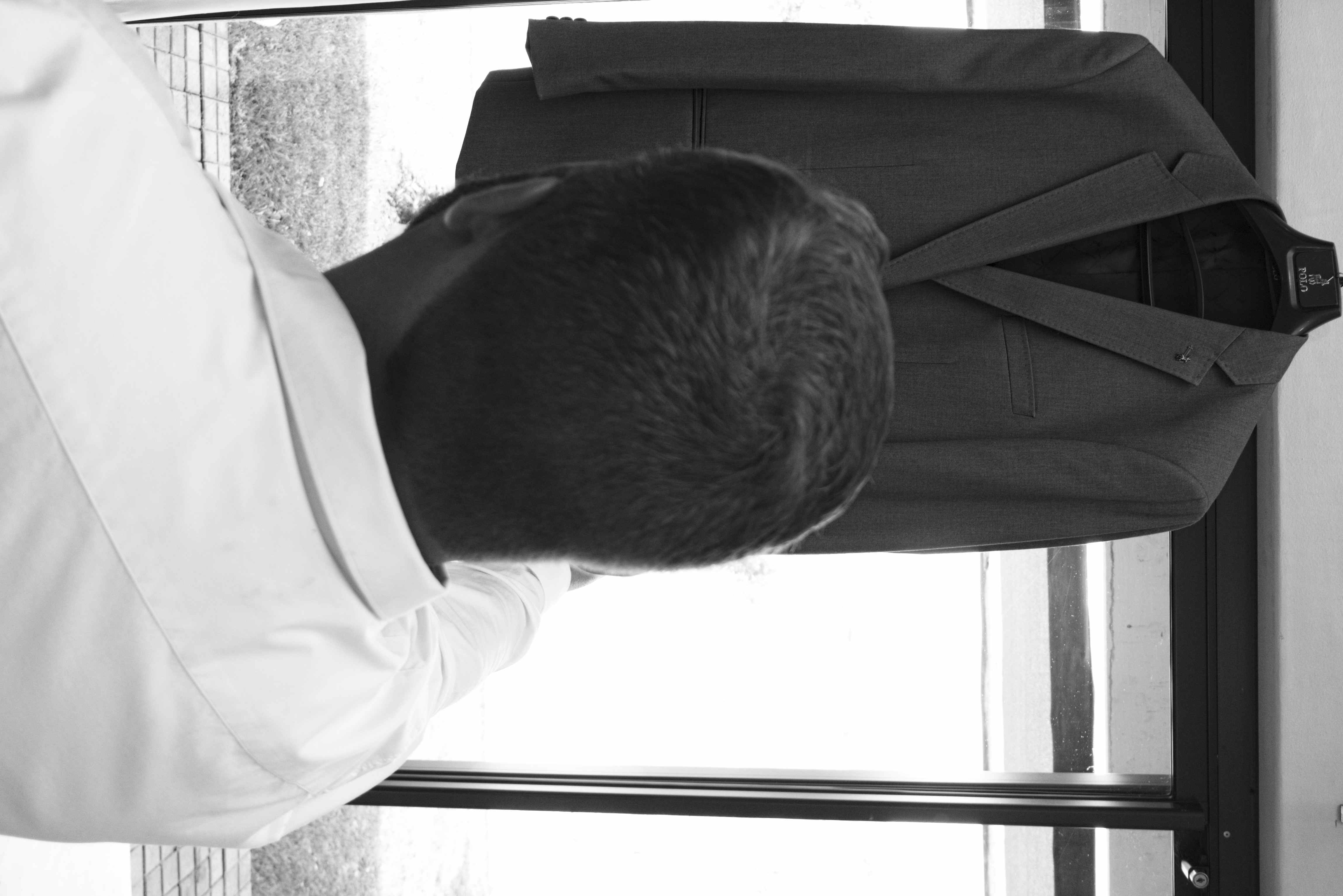 Black and white image of the groom reaching for his hanging suit jacket