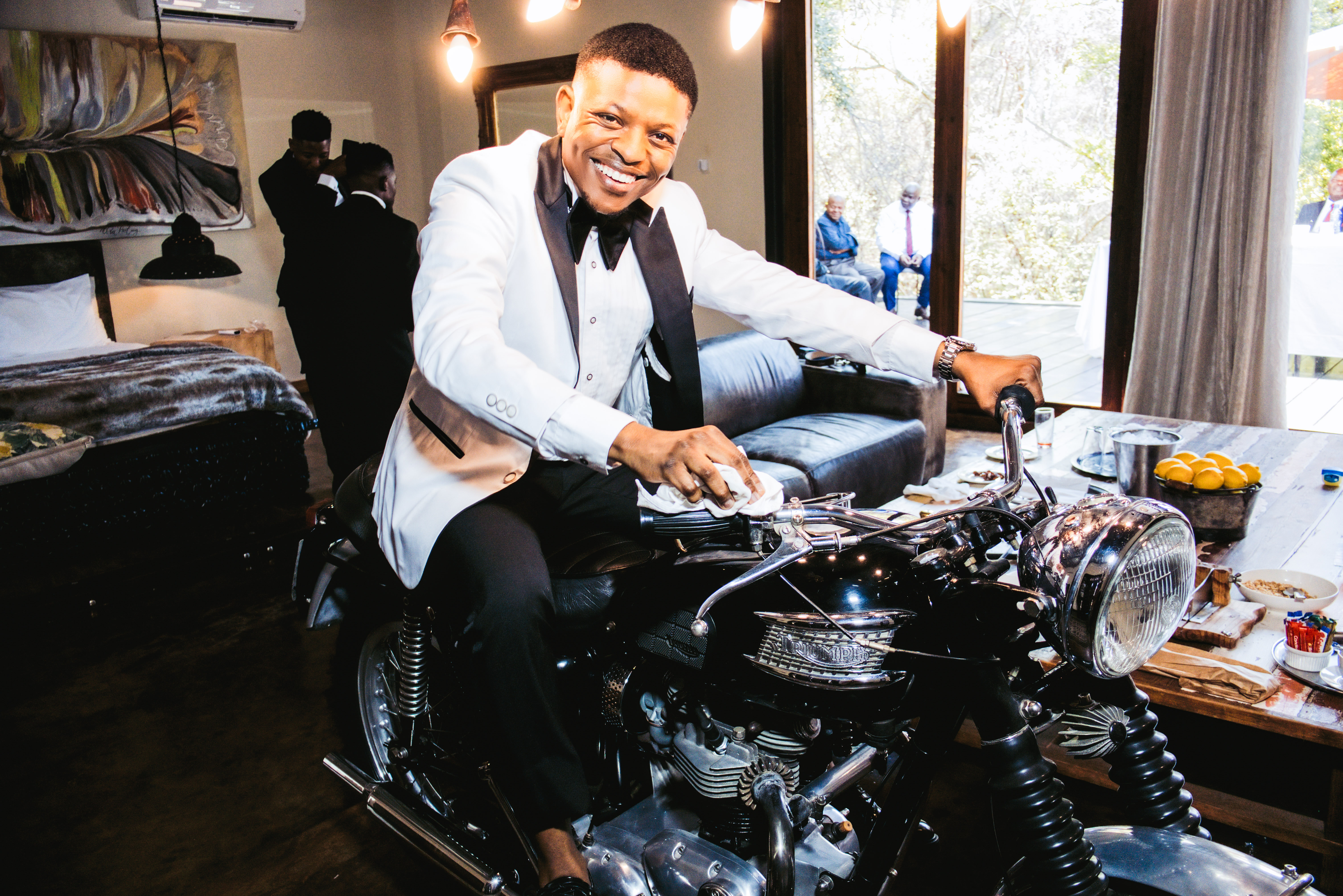 Smiling groom in a white tuxedo on a vintage motorcycle