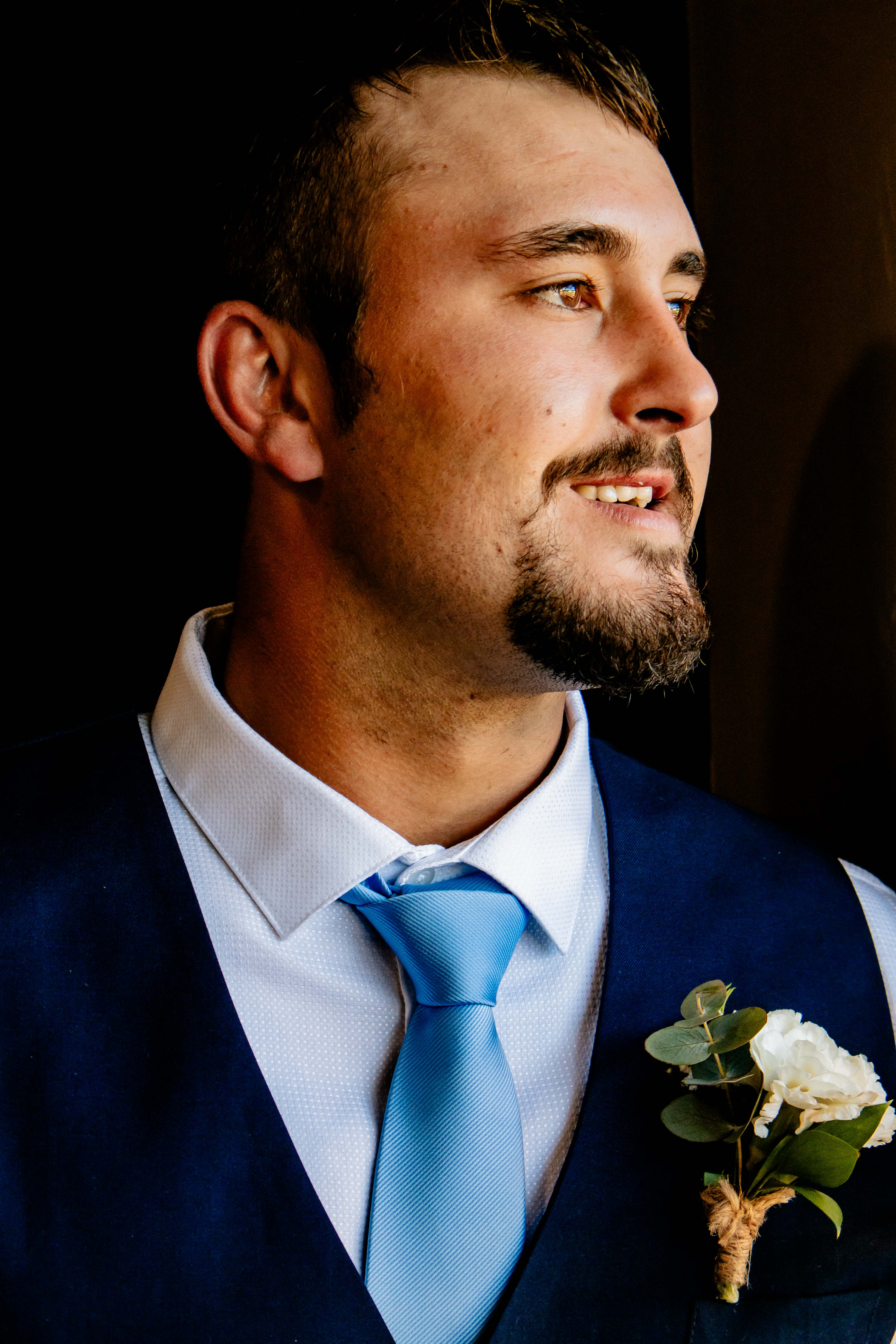 Groom in a navy waistcoat and blue tie lit by window light