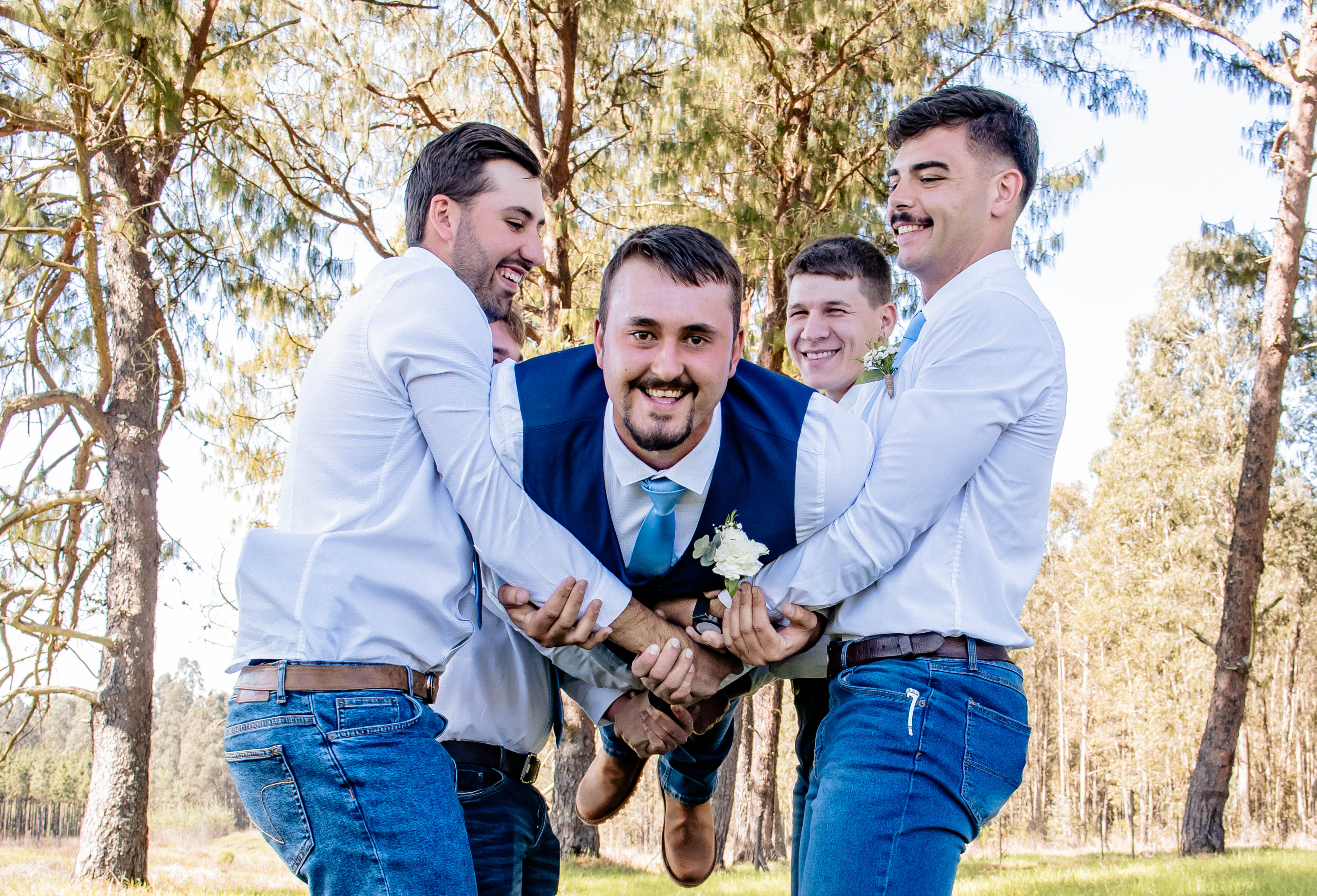 Groomsmen playfully lifting the groom among the trees