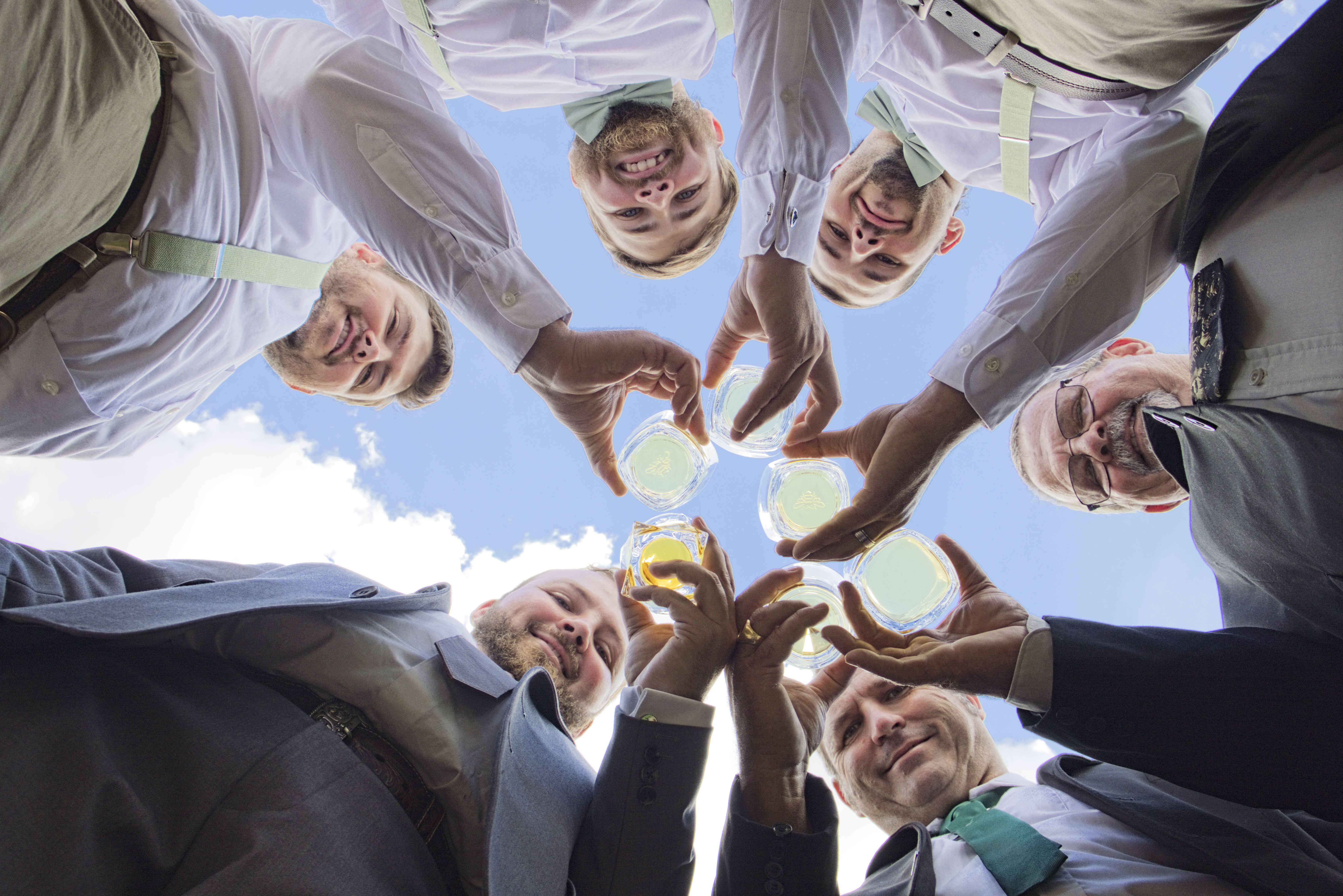 Groomsmen raising a toast, photographed from below against a blue sky