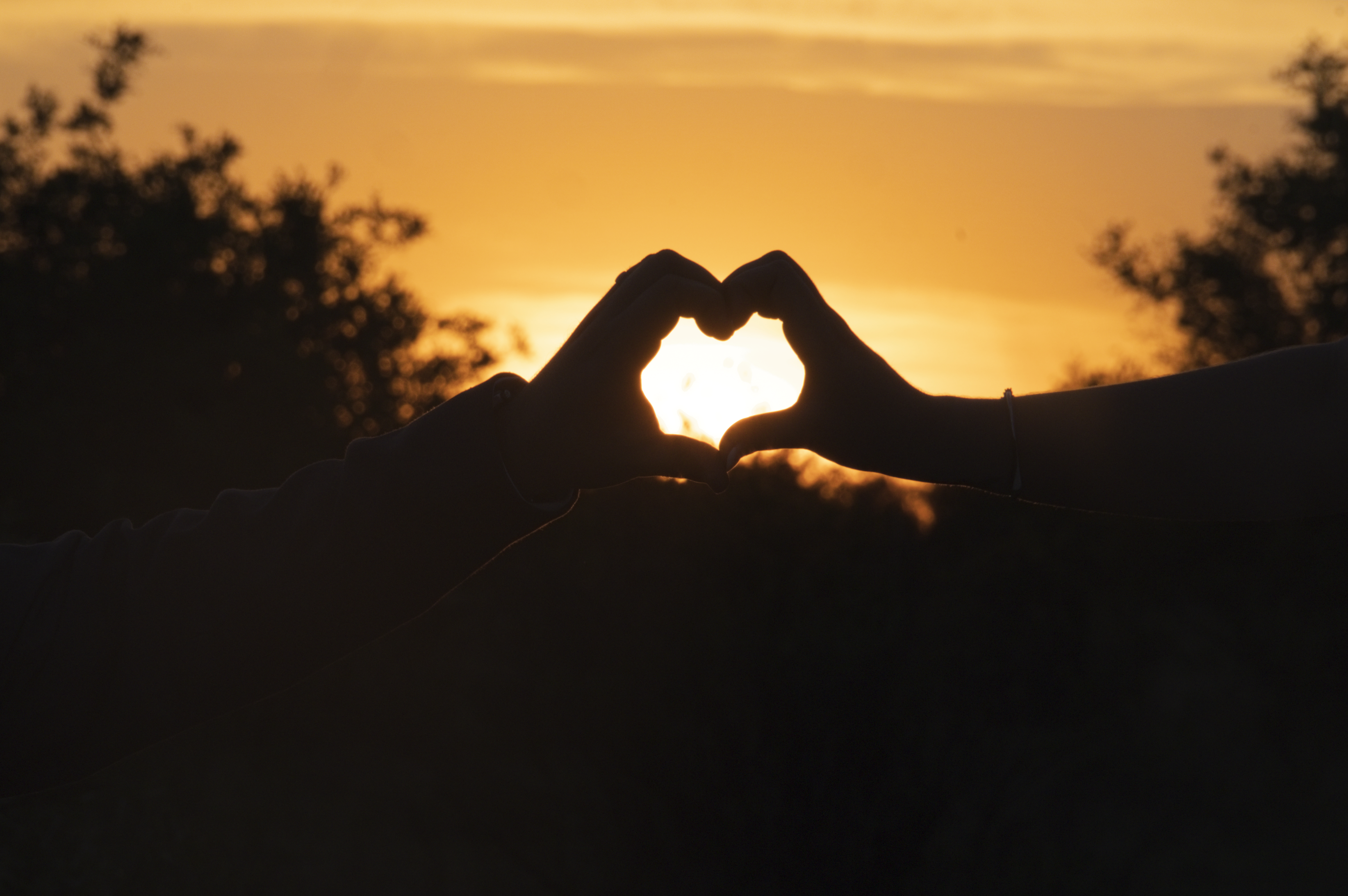Silhouetted hands forming a heart around the setting sun
