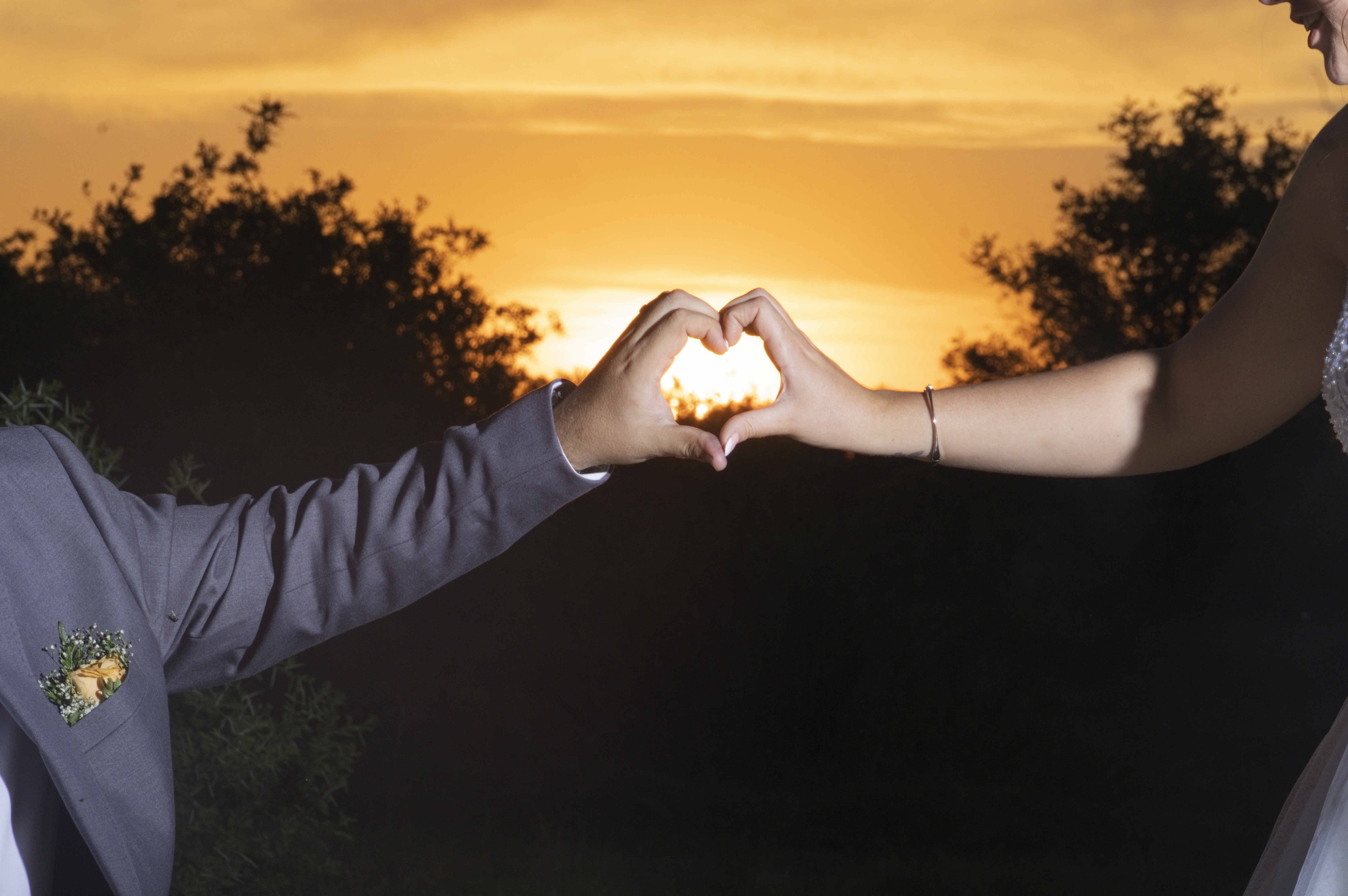 Close-up of heart hands framing the sunset