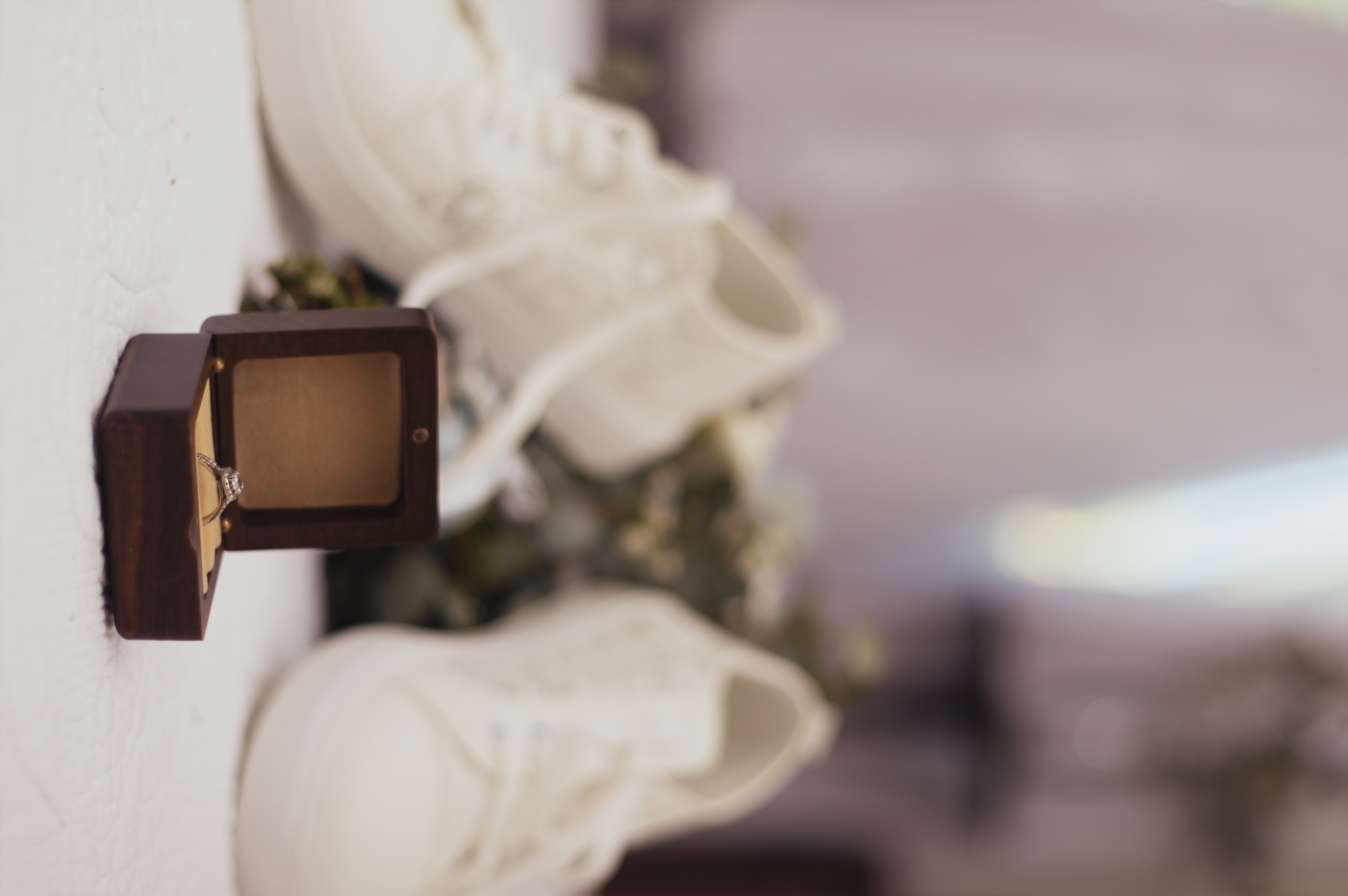 Engagement ring in a wooden box with bridal sneakers behind