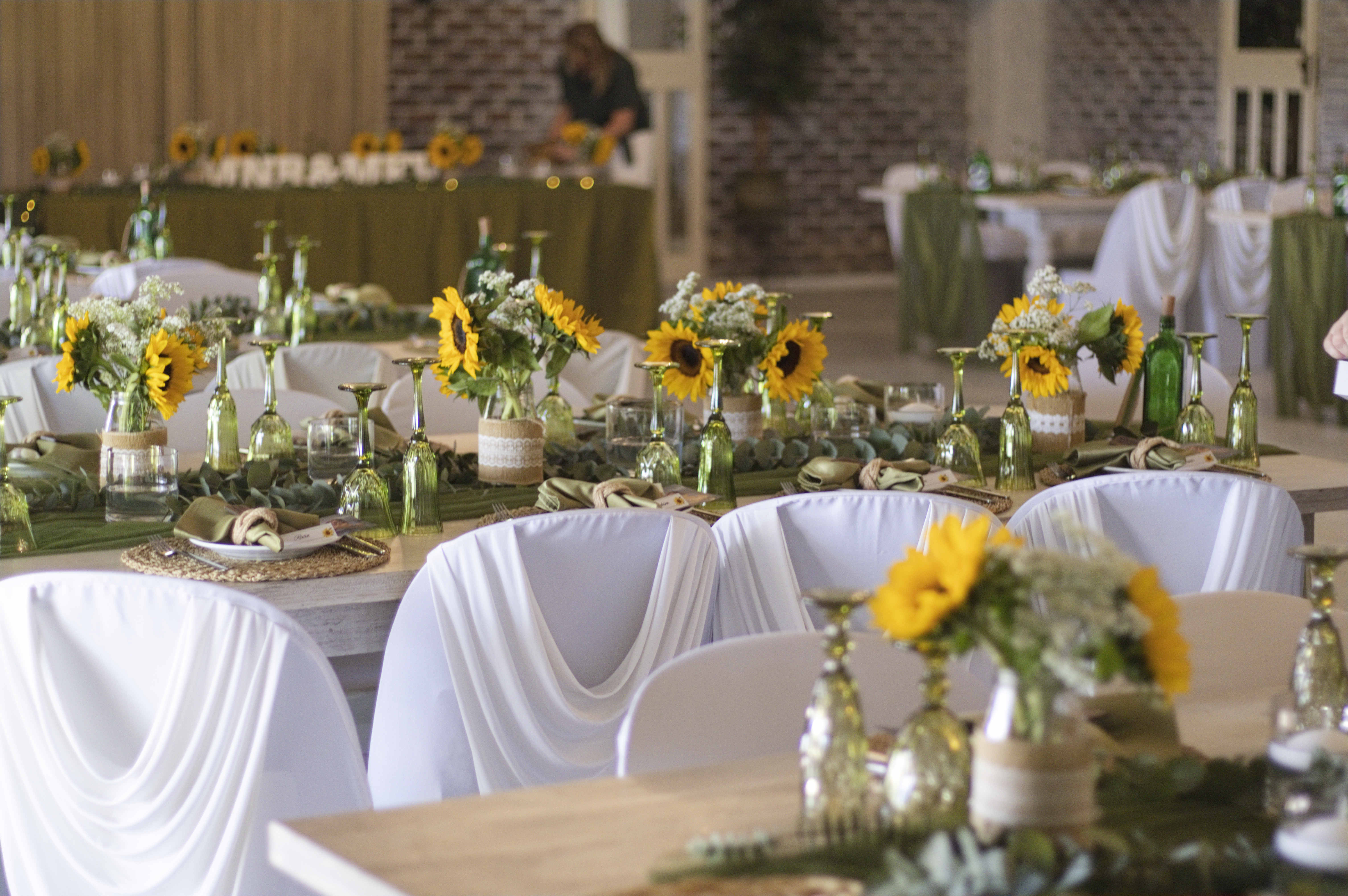 Reception hall styled with sunflowers, green glassware and draped white chairs