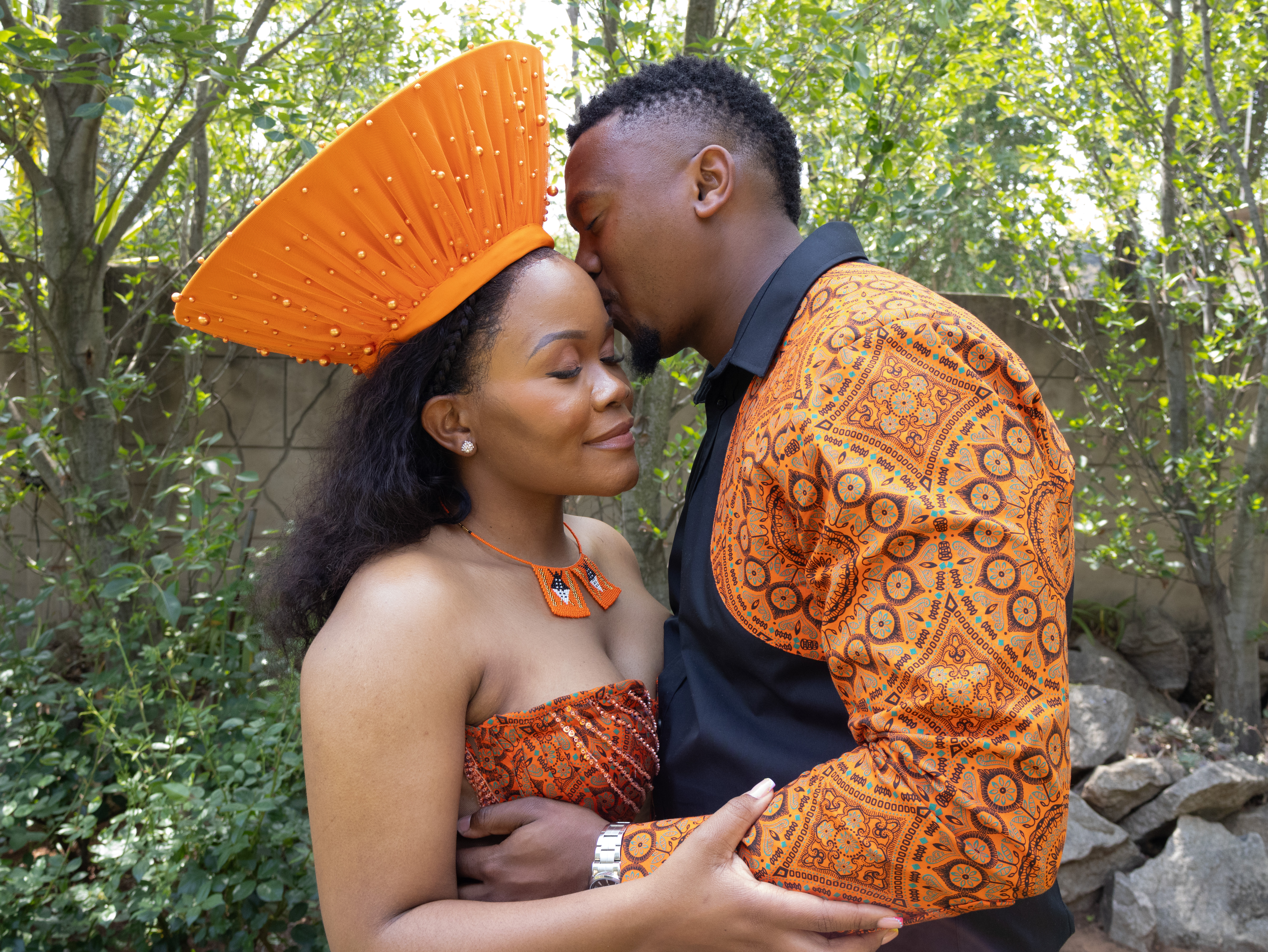 Groom kissing the bride's forehead in traditional orange attire and headdress